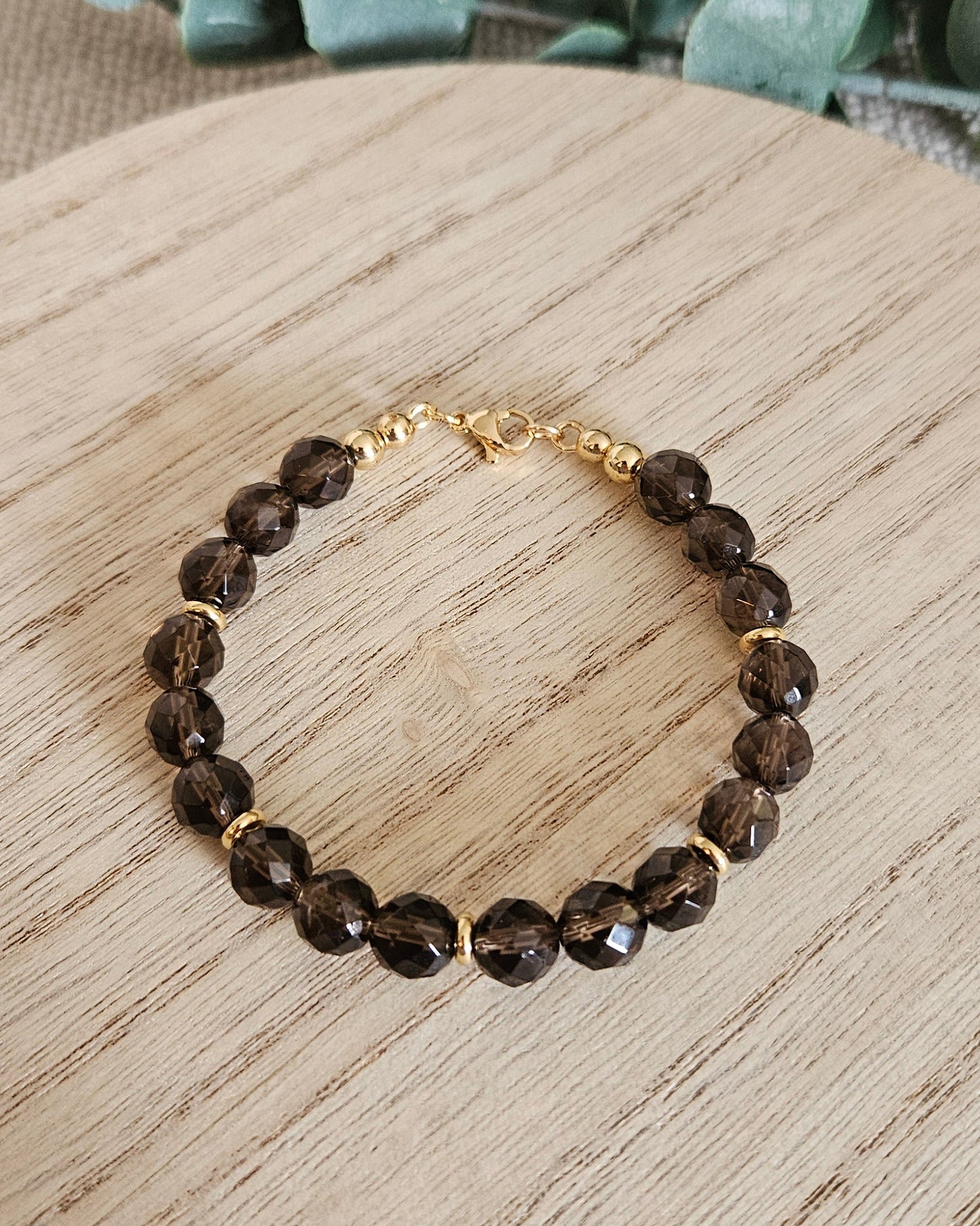 Brown beaded bracelet on a wooden surface with green leaves in the background