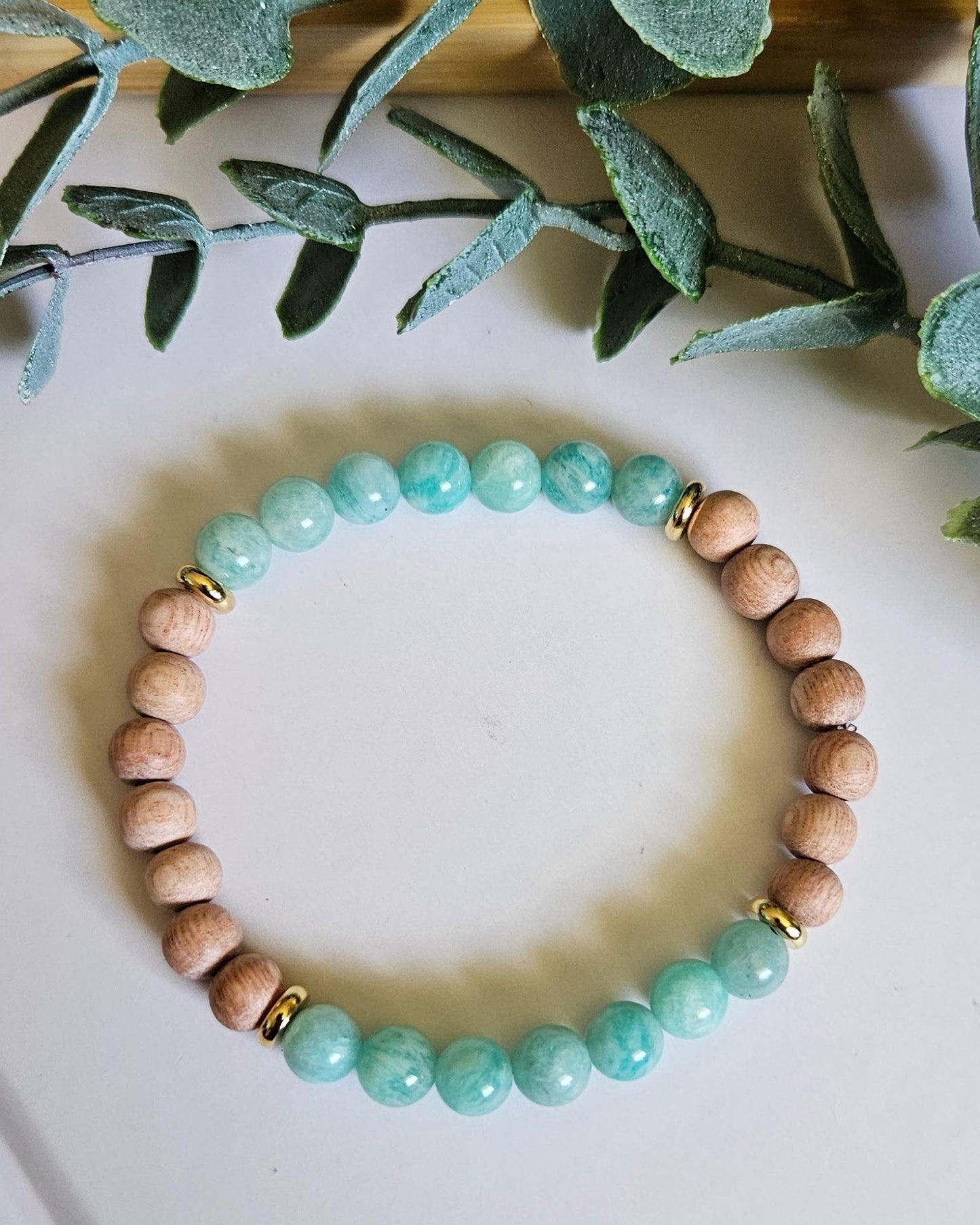 Beaded bracelet with turquoise and beige beads on a white surface with green leaves.