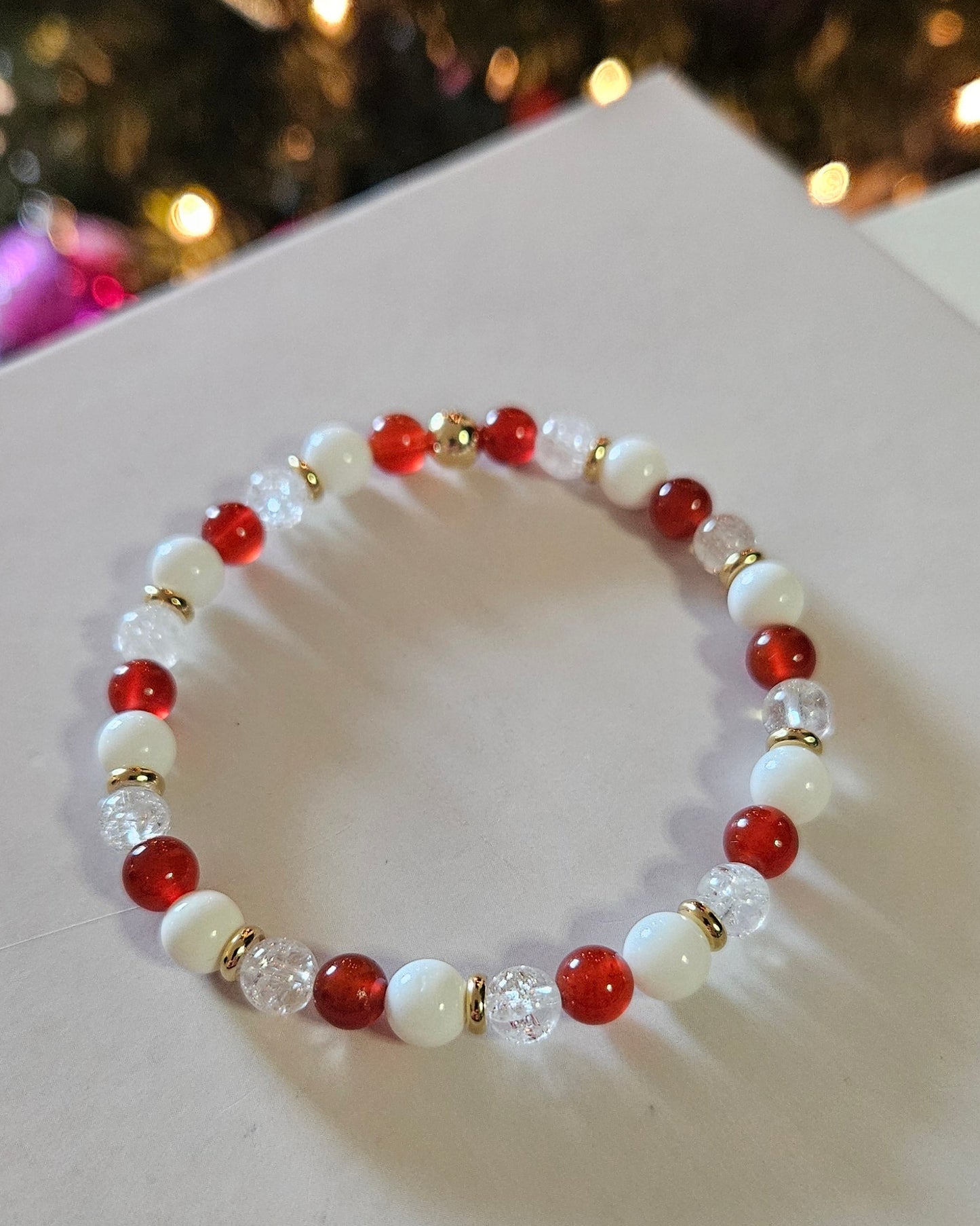Beaded bracelet with red and white beads on a white card, Christmas tree in the background