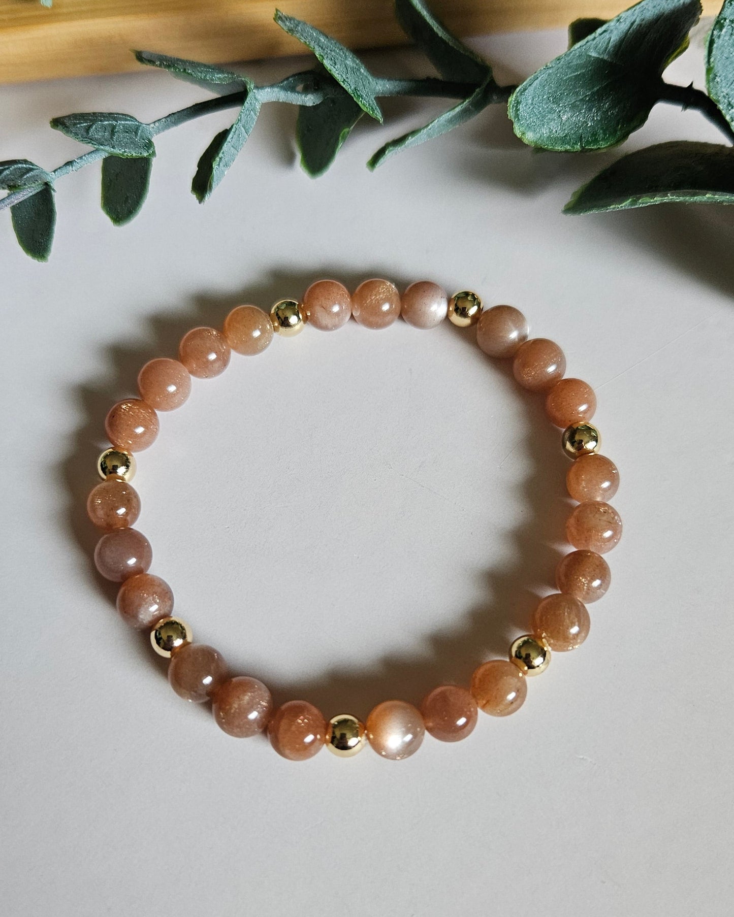 sunstone bracelet with gold accents on a light surface with green leaves