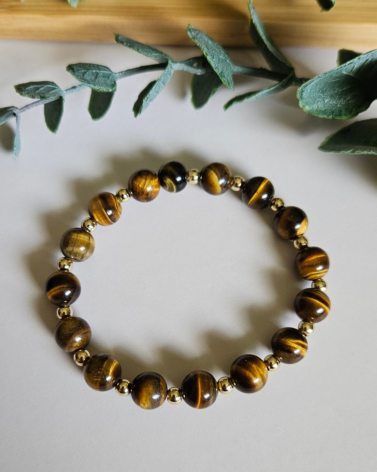 Bracelet with tiger eye beads on a white surface with green leaves