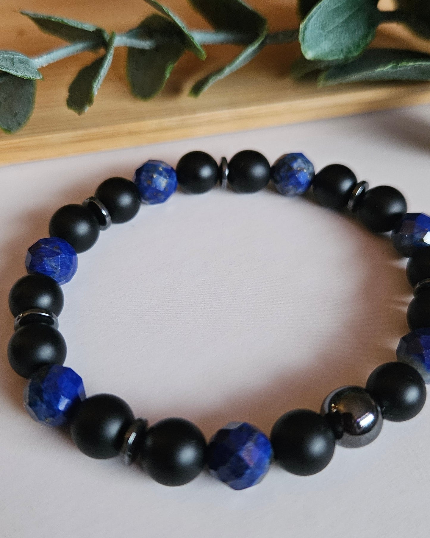 Black and blue beaded bracelet on a white surface with green leaves in the background