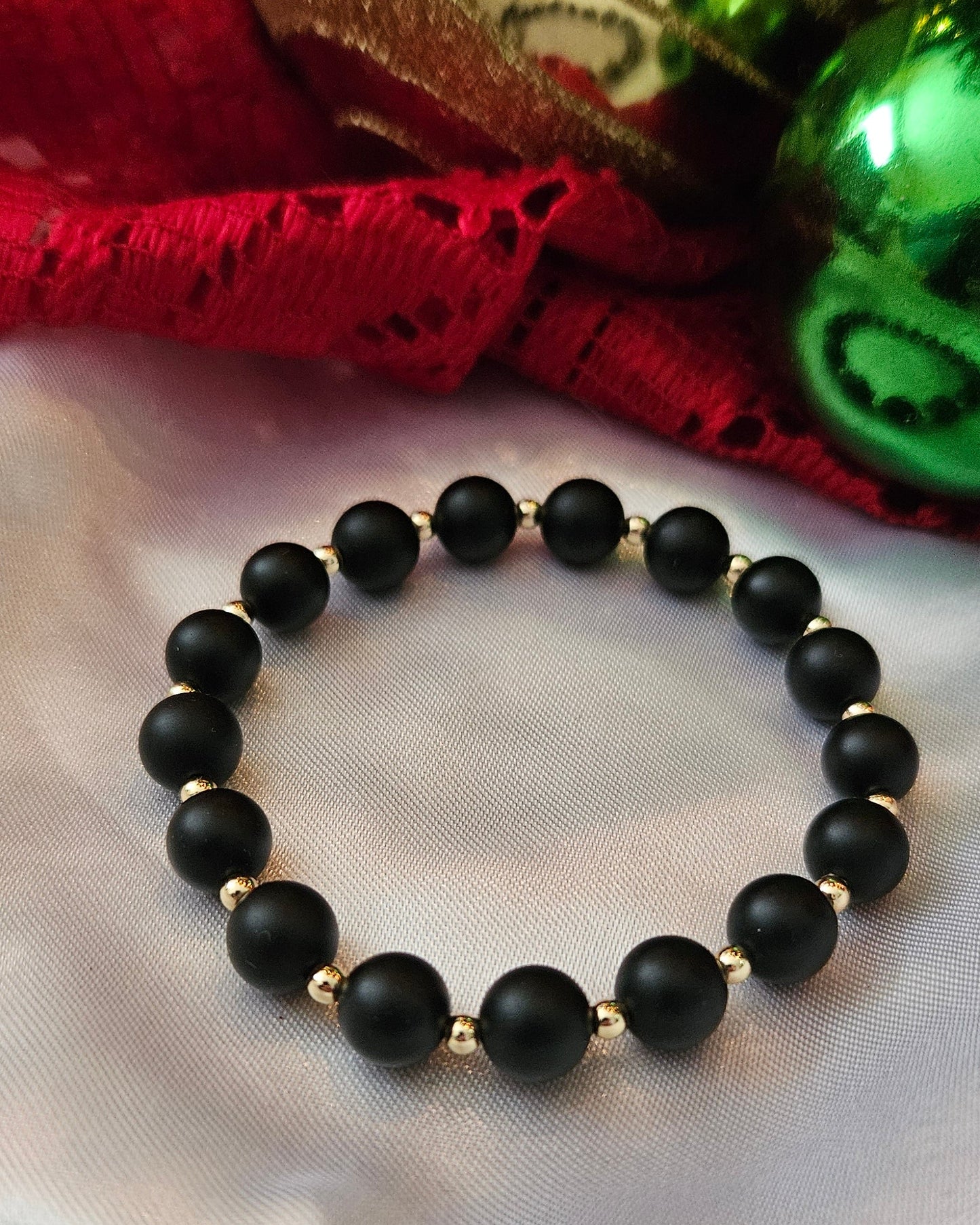 Black beaded bracelet on a textured white surface with decorative items.