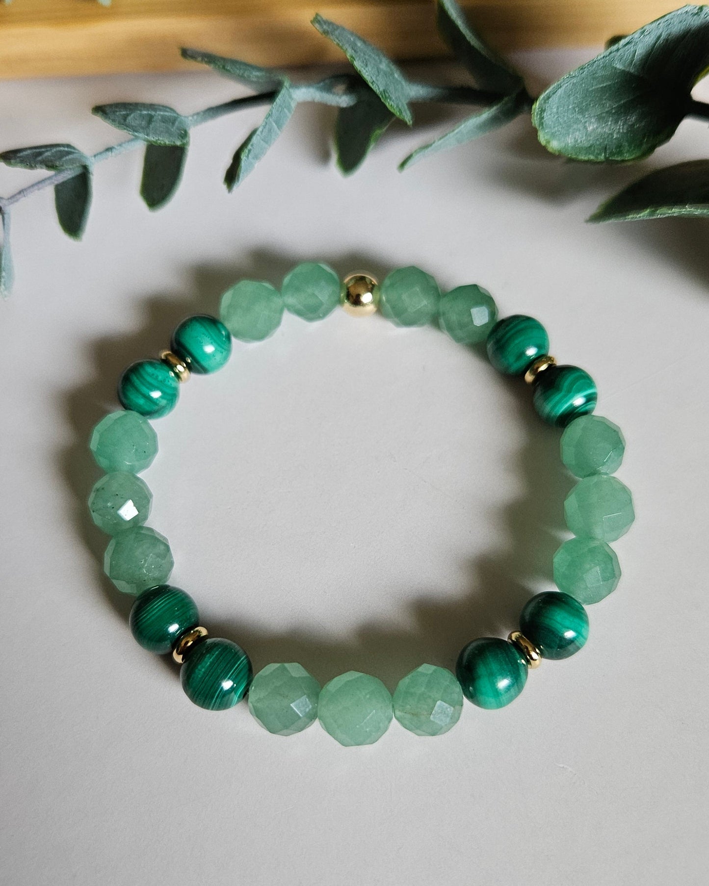 Green beaded bracelet on a white surface with green leaves in the background