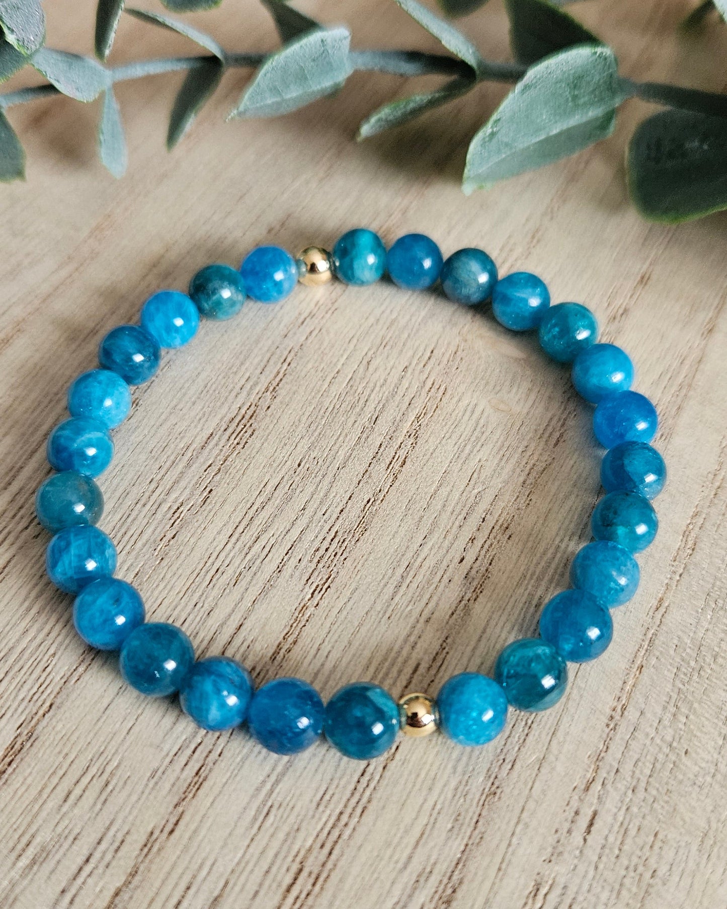 Blue beaded bracelet on a wooden surface with green leaves