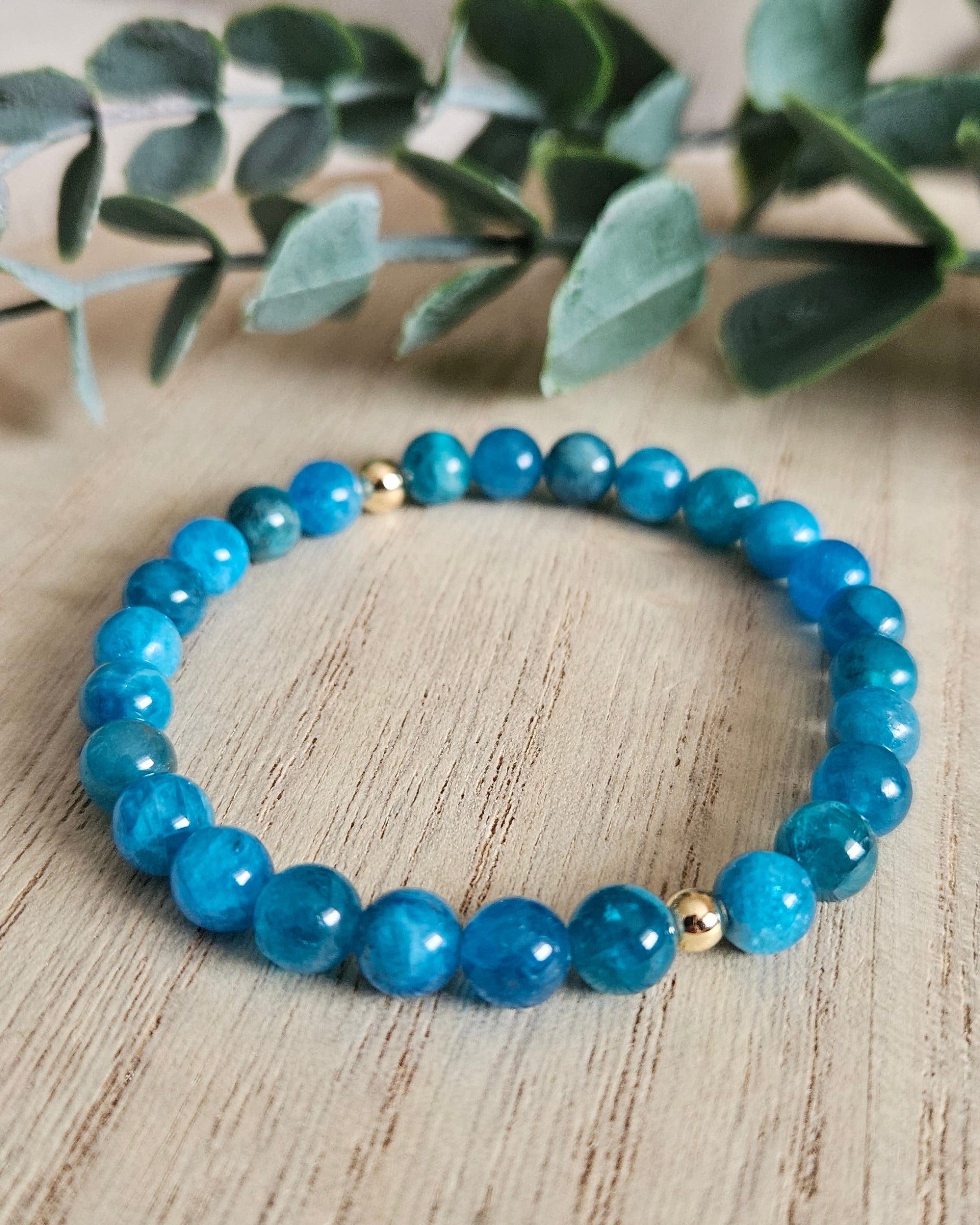 Blue beaded bracelet on a wooden surface with a plant in the background