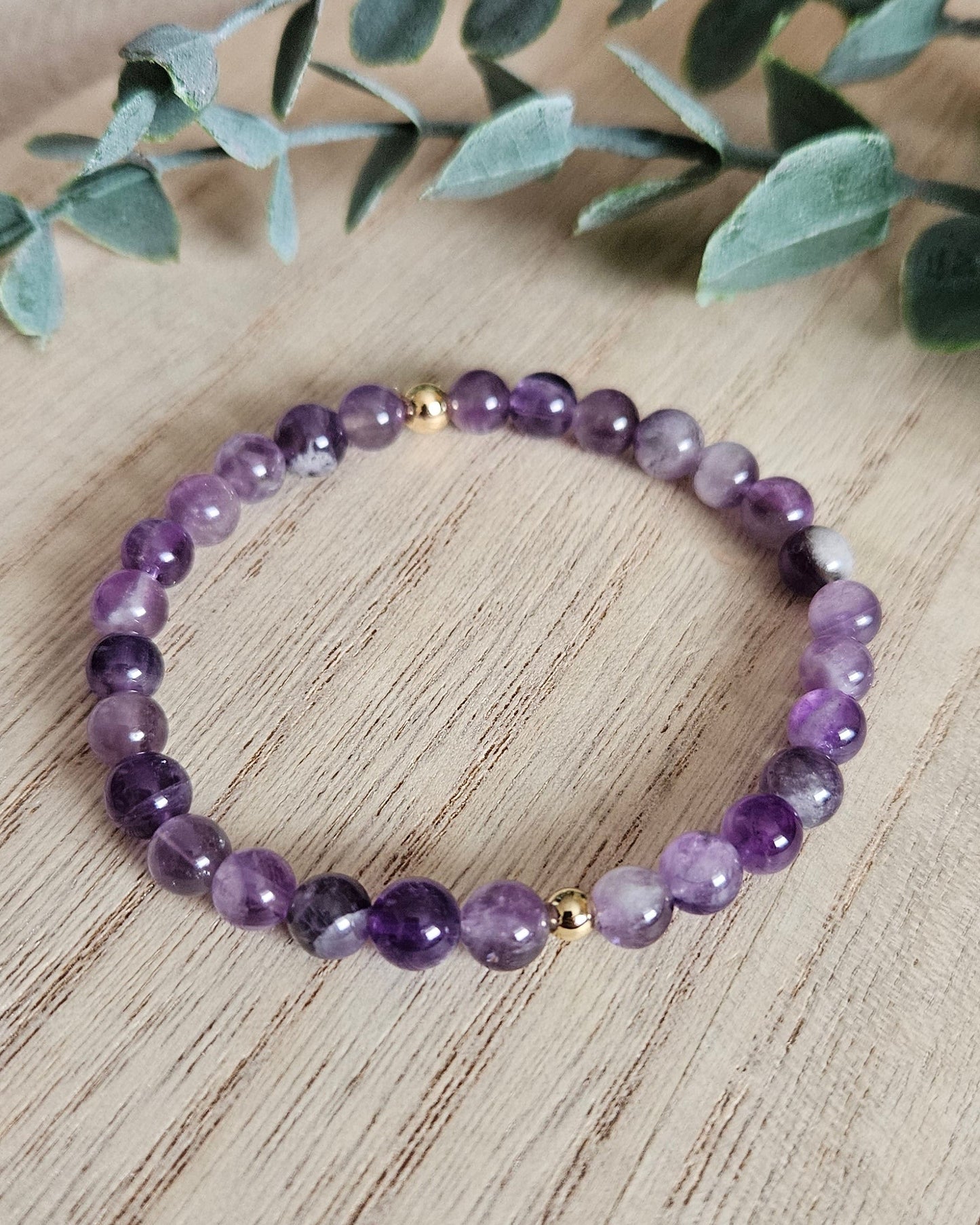 Purple beaded bracelet on a wooden surface with green leaves