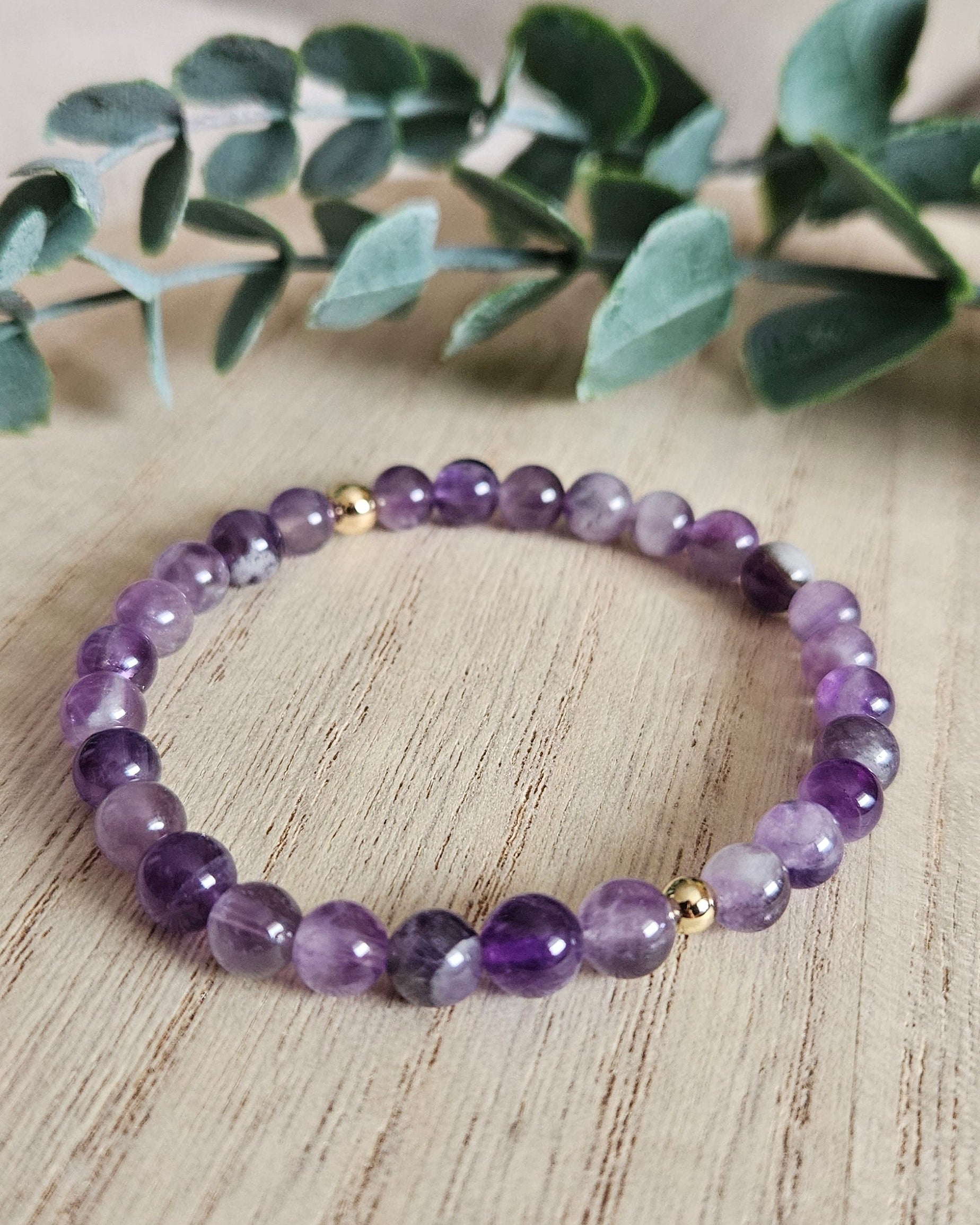 Amethyst bracelet on a wooden surface with greenery