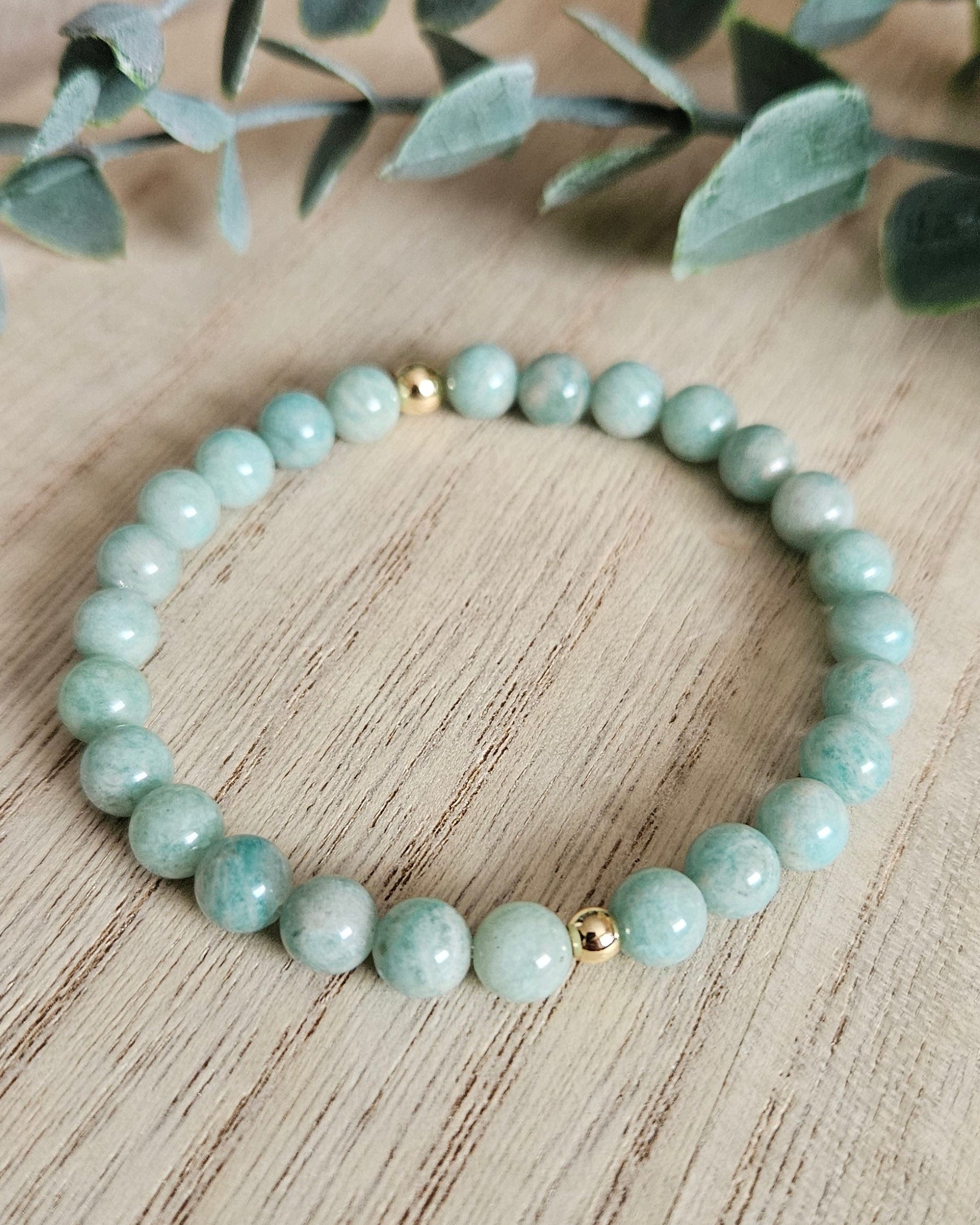 Light blue beaded bracelet on a wooden surface with green leaves.
