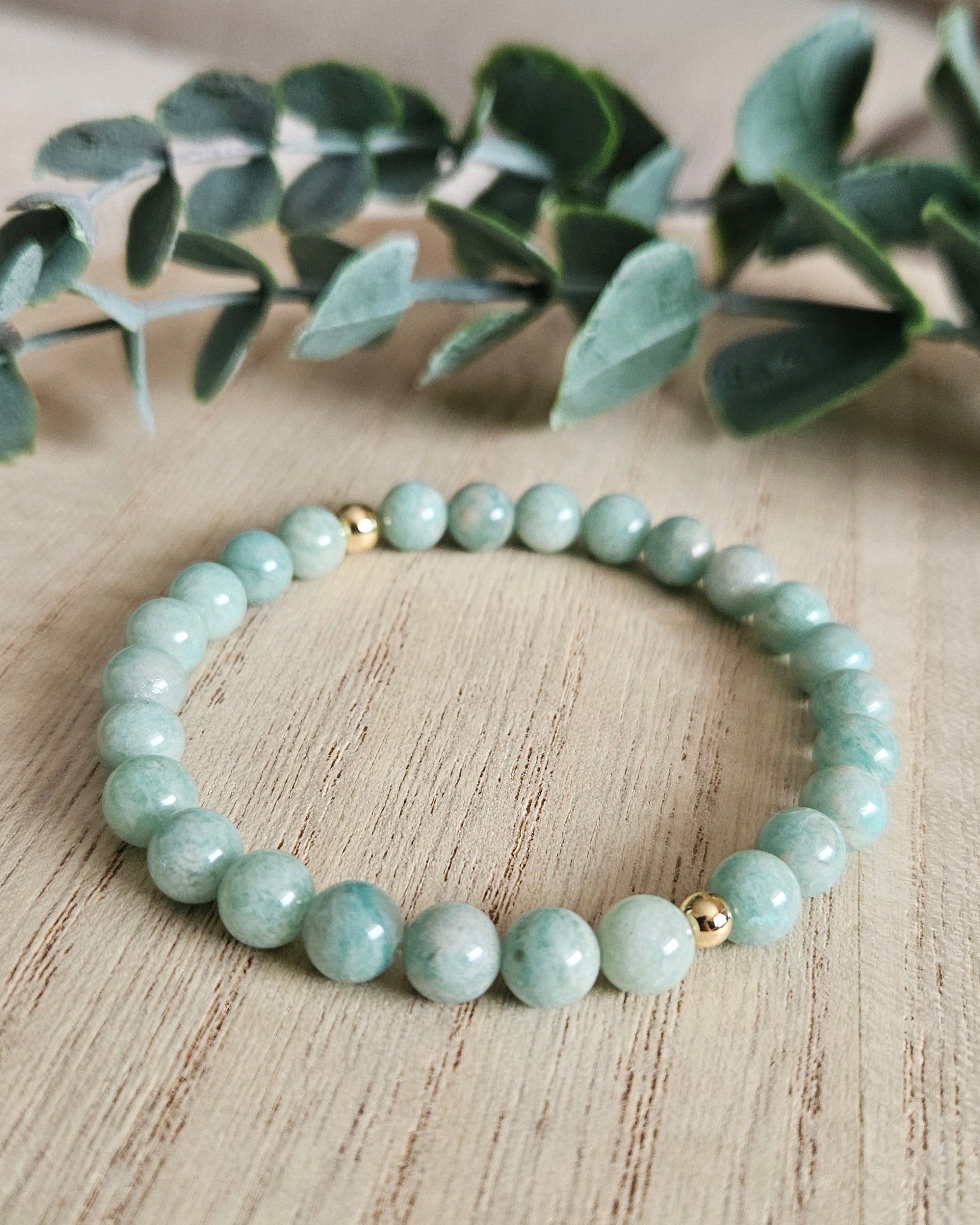 Green beaded bracelet on a wooden surface with greenery