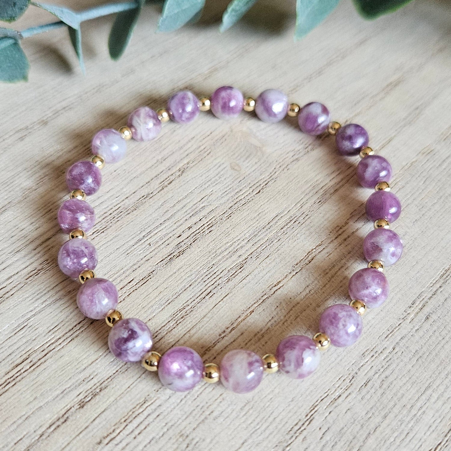Purple beaded bracelet on a wooden surface with green leaves