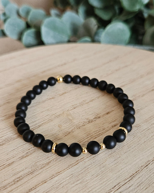 Black beaded bracelet on a wooden surface with greenery in the background