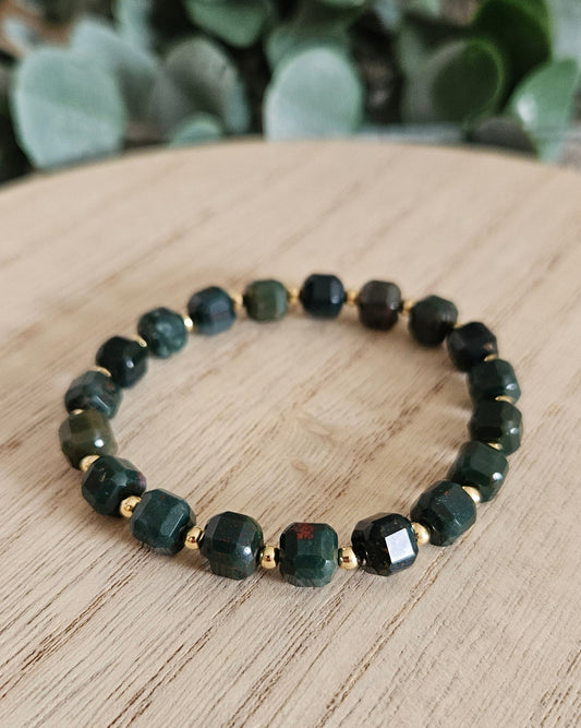 Green beaded bracelet on a wooden surface with greenery in the background