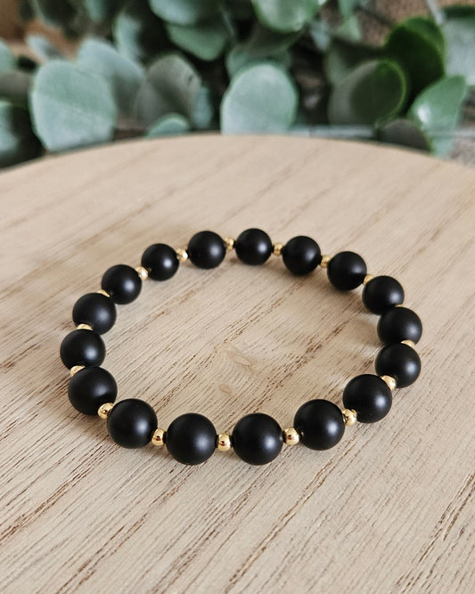 Black beaded bracelet on a wooden surface with green leaves in the background