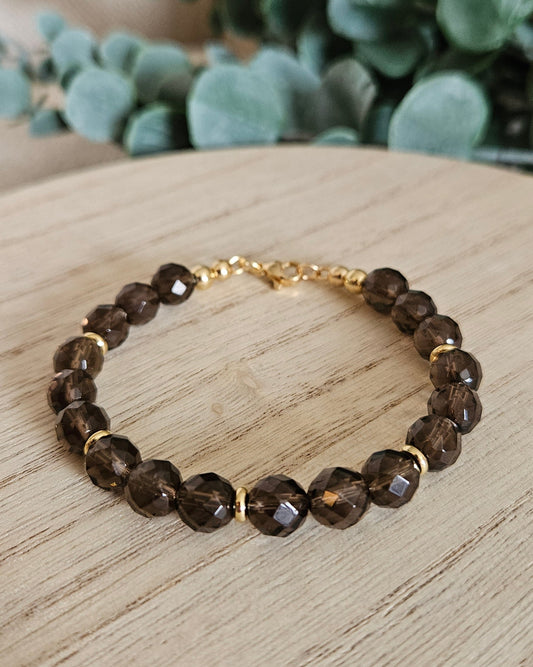 Brown beaded bracelet with gold accents on a wooden surface with greenery in the background