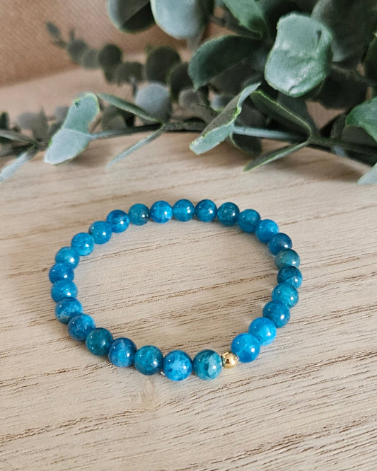 Blue beaded bracelet on a wooden surface with green leaves in the background
