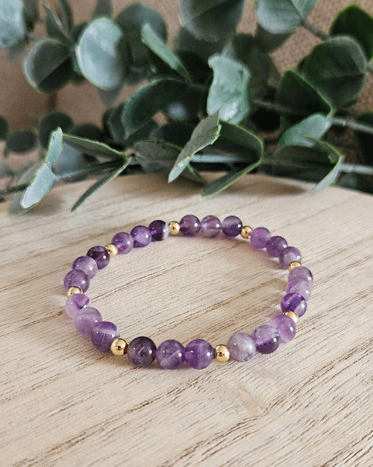 Purple beaded bracelet on a wooden surface with green leaves in the background