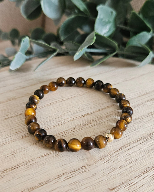 Tiger eye beaded bracelet on a wooden surface with a plant in the background