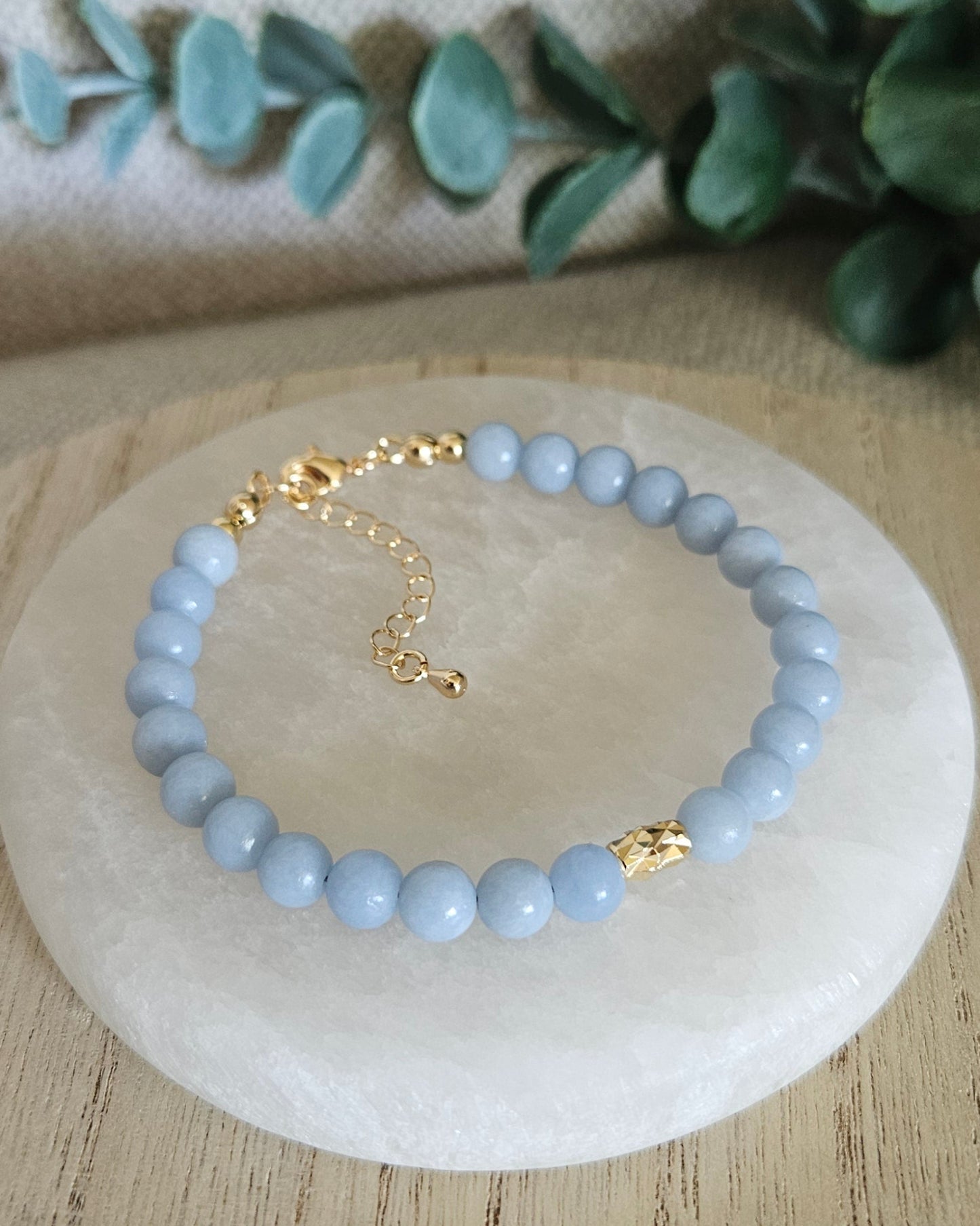 Light blue beaded bracelet on a white stone with greenery in the background