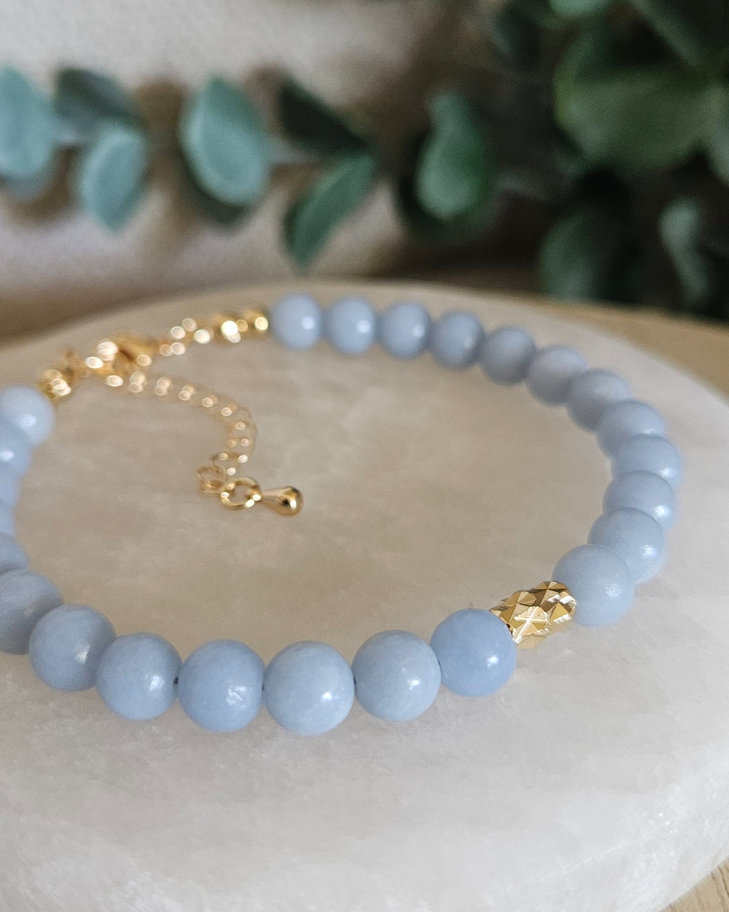 Light blue beaded bracelet with gold accents on a white stone surface with greenery in the background