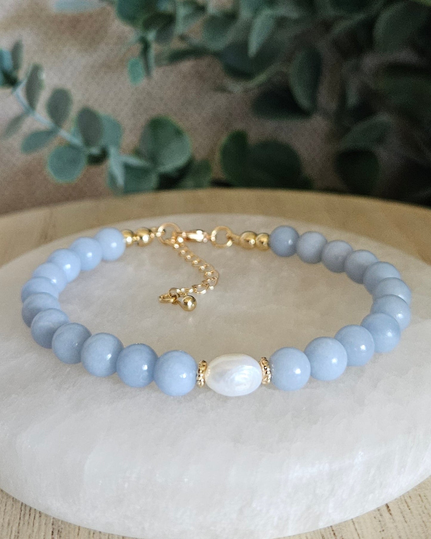Blue beaded bracelet with a gold charm on a white stone surface with greenery in the background