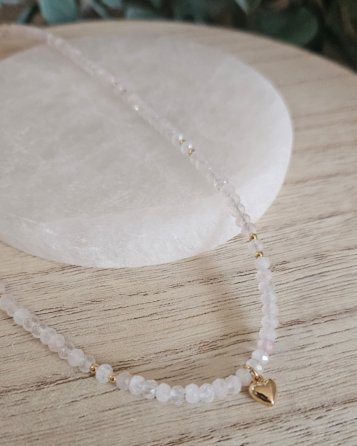 Angled close view of the Rose Quartz rondelle necklace and polished gold-plated heart pendant