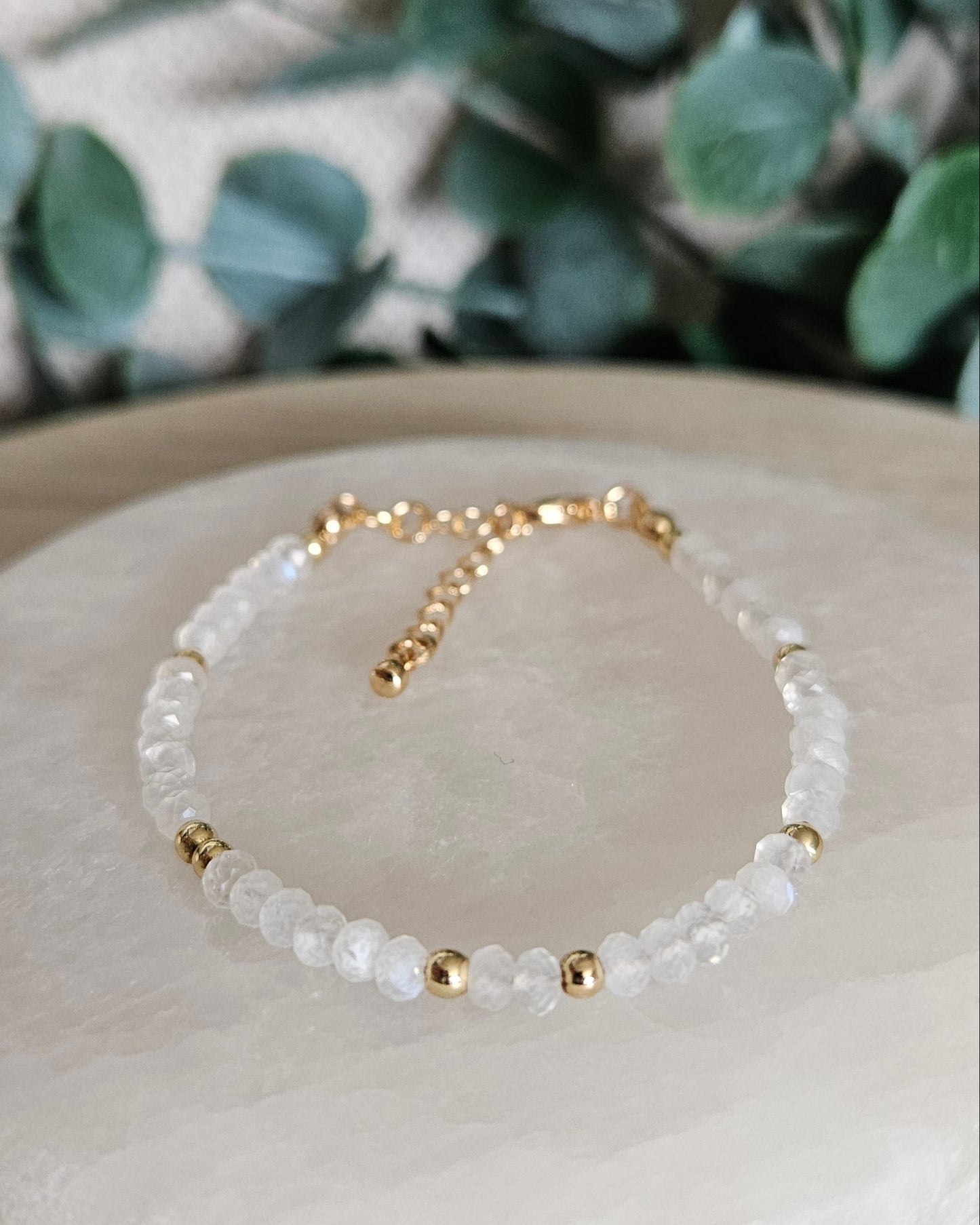 Angled view of the delicate Moonstone rondelle bracelet and gold accents displayed on a selenite plate