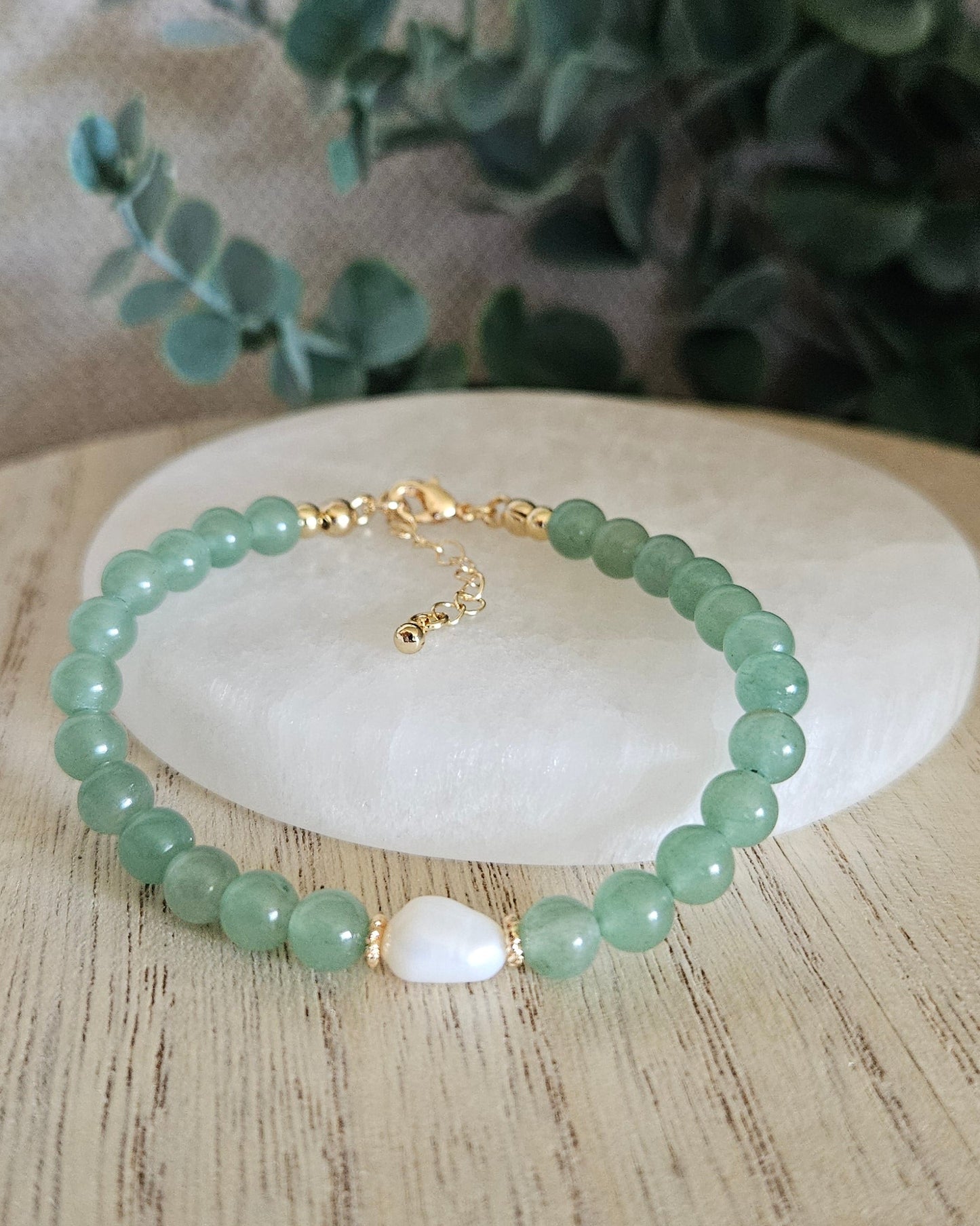 Green beaded bracelet on a white stone with greenery in the background
