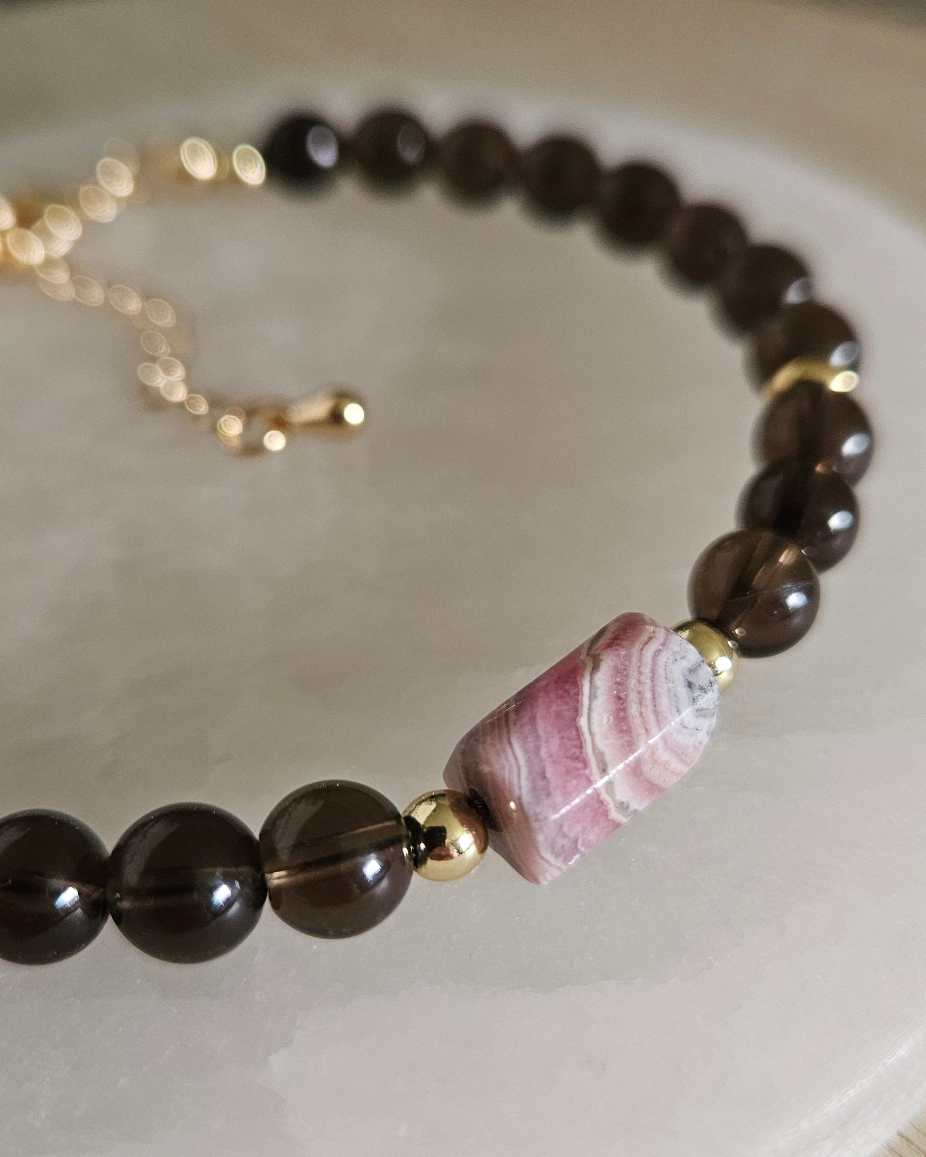 Close-up of the pink-and-white banded Rhodochrosite focal, translucent Smoky Quartz beads and gold accents