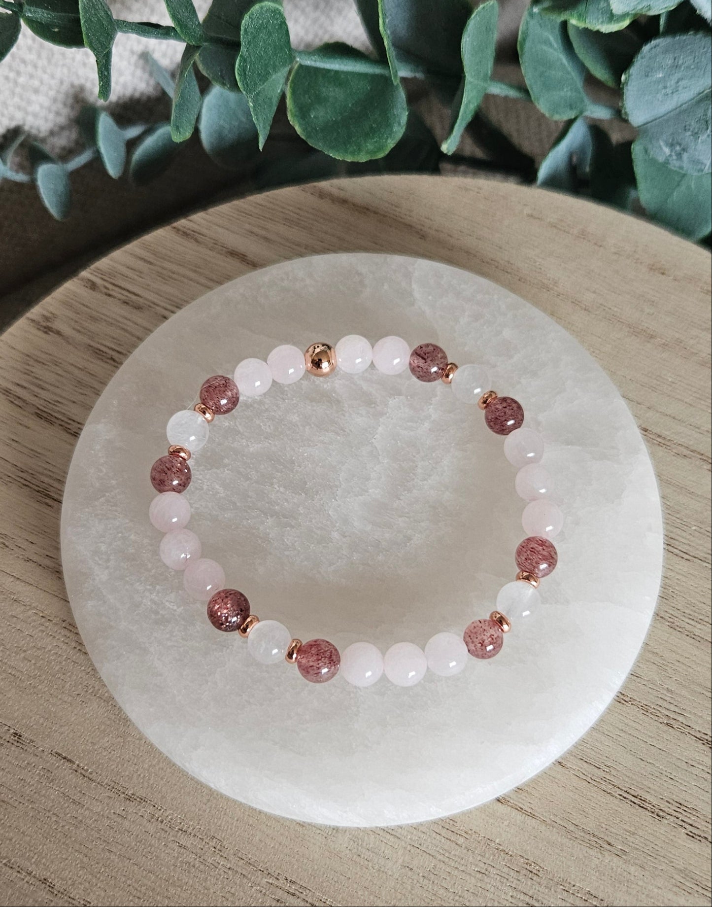 Close-up of pale Rose Quartz, white Moonstone and sparkling Strawberry Quartz beads beside leafy greenery