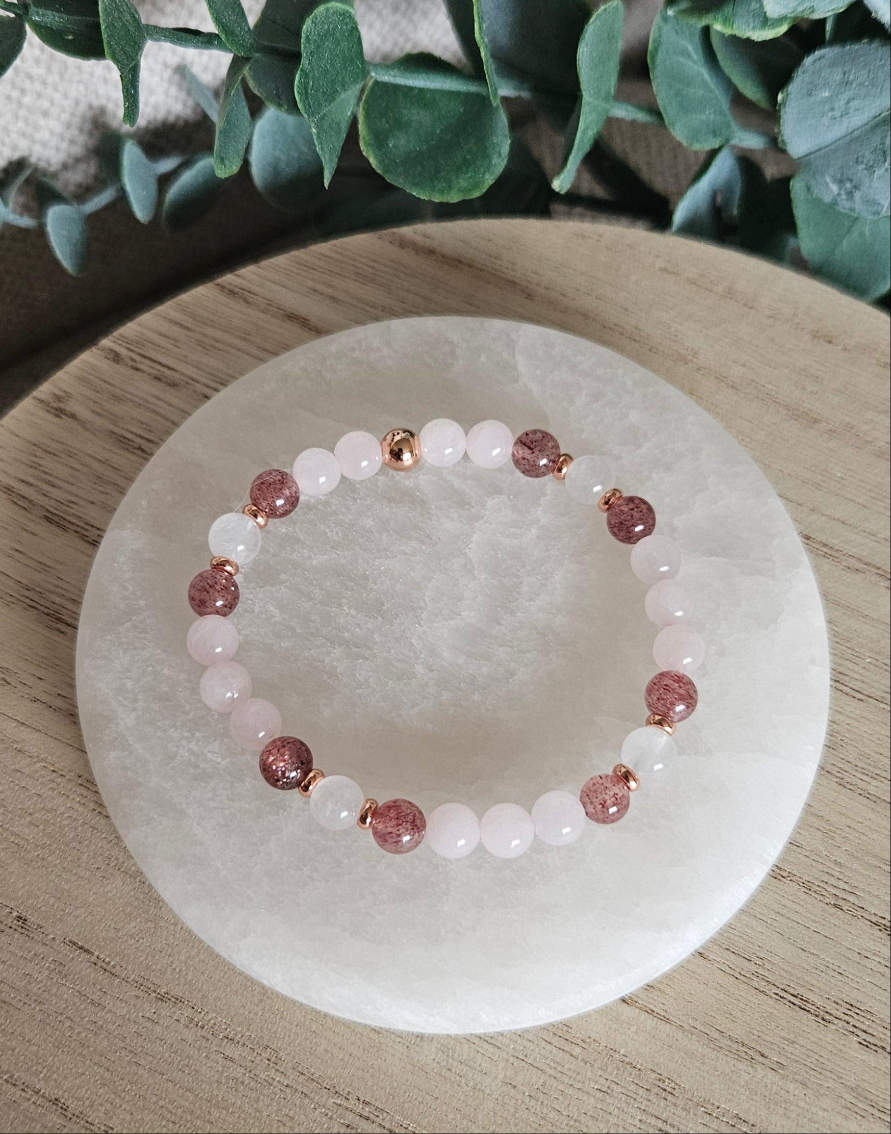 Close-up of pale Rose Quartz, white Moonstone and sparkling Strawberry Quartz beads beside leafy greenery