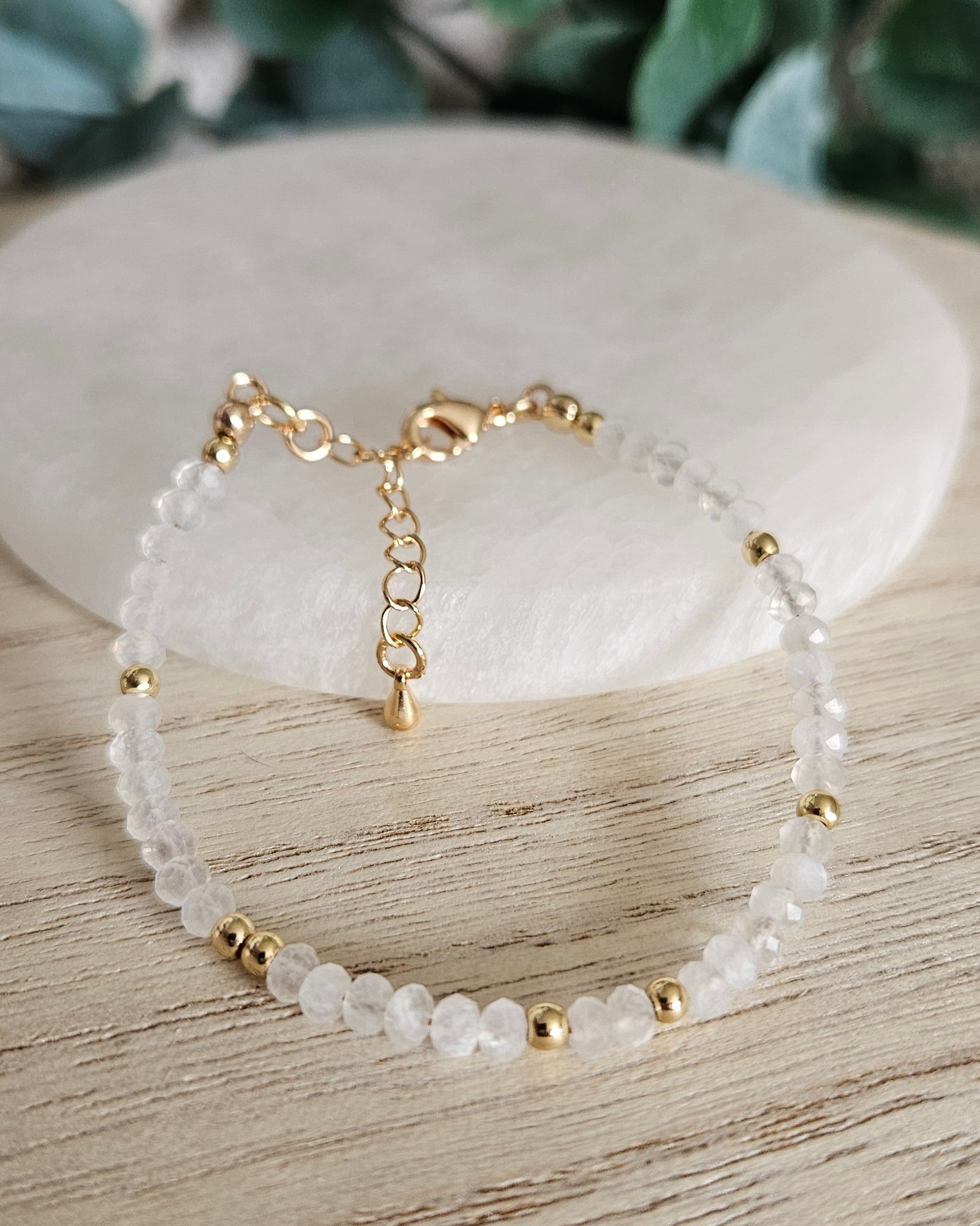 Faceted Moonstone rondelle bracelet with gold-plated accents, clasp and extender chain arranged before selenite