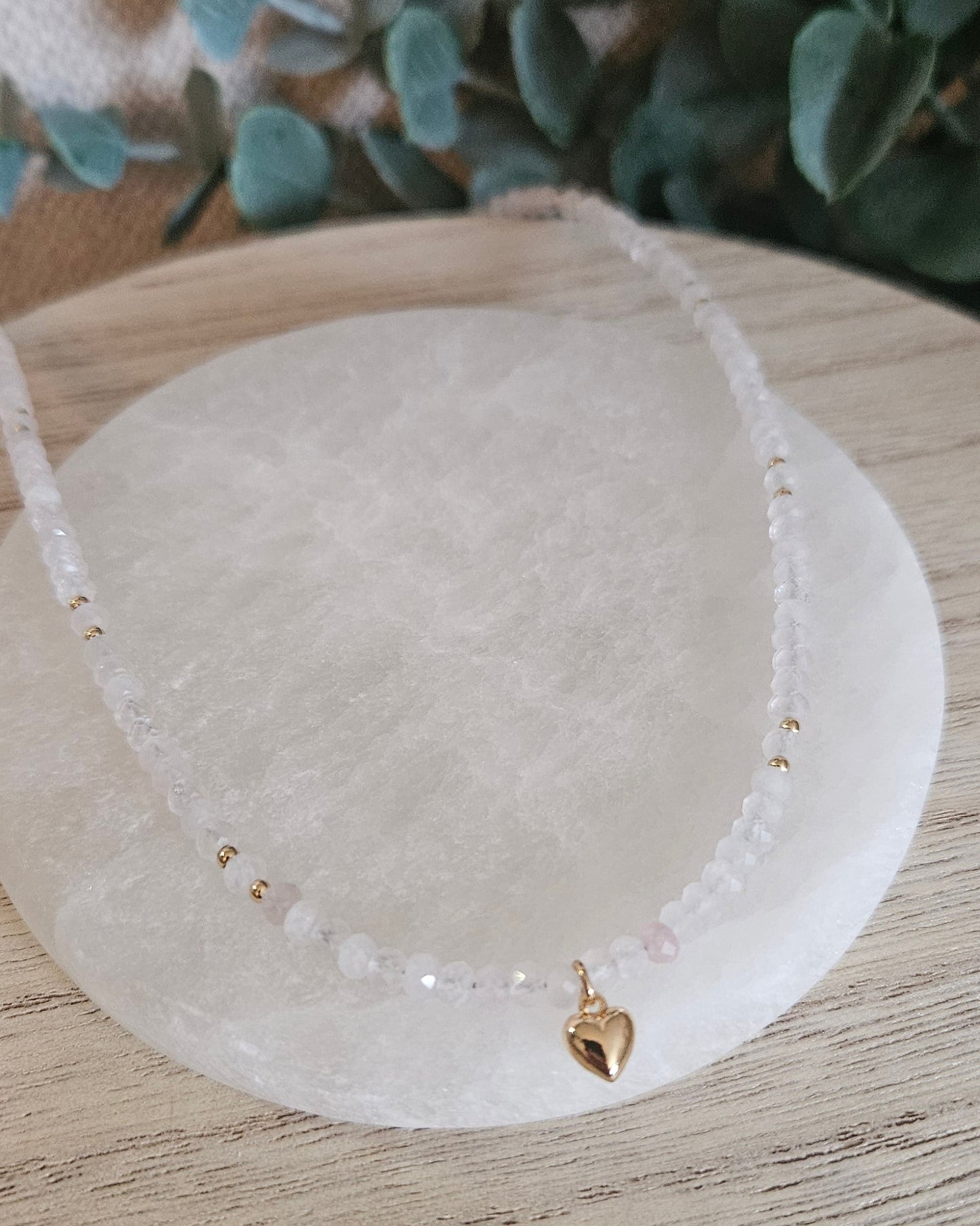 Faceted Rose Quartz necklace with gold-plated heart pendant draped across a round selenite plate