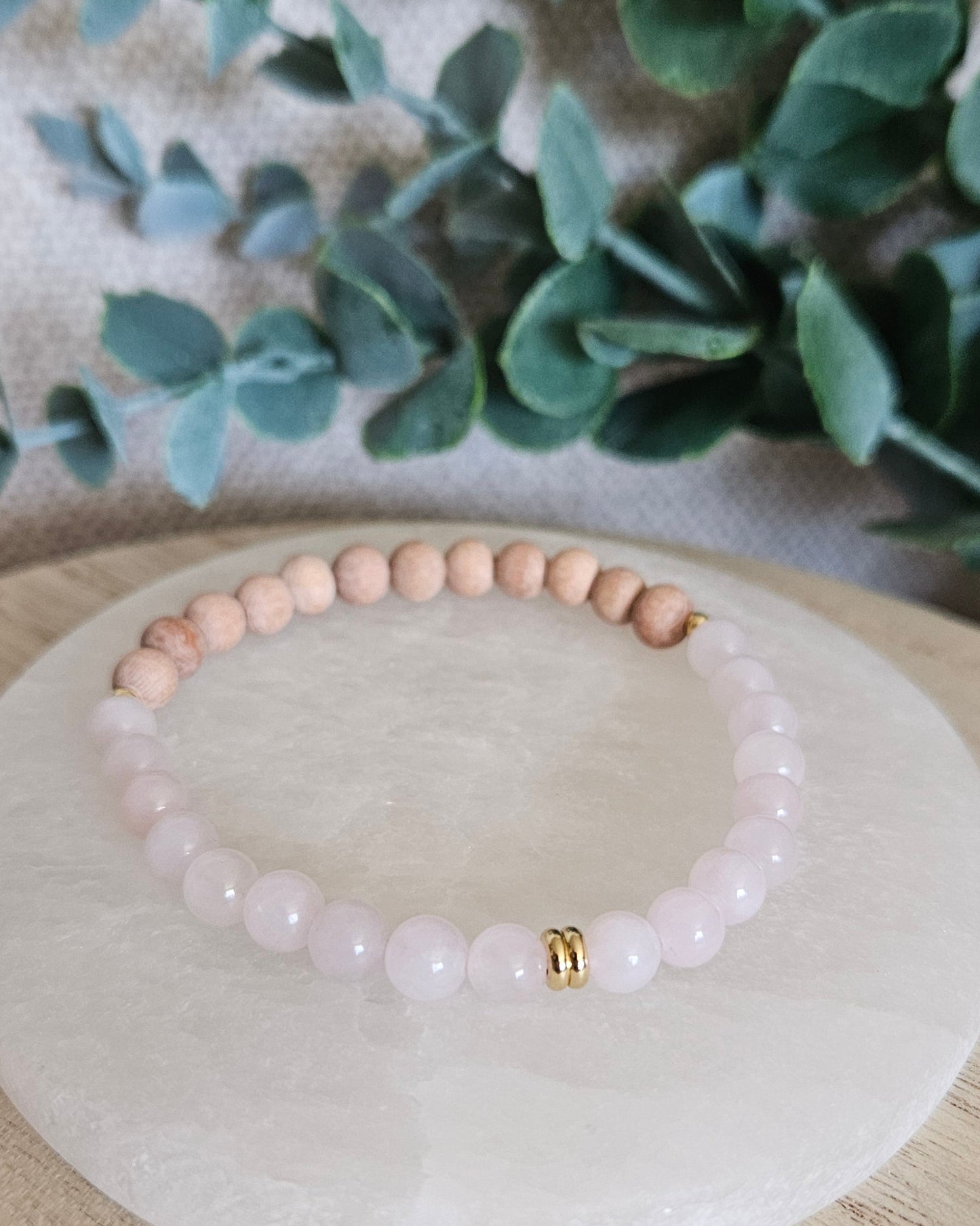 Front view of the Rose Quartz and Rosewood stretch bracelet arranged on a round selenite plate