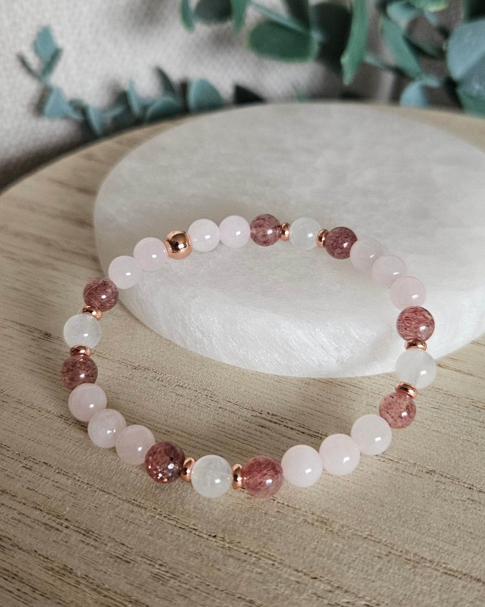 Full Rose Quartz, Moonstone and Strawberry Quartz stretch bracelet with rose gold-plated accents on a wooden surface