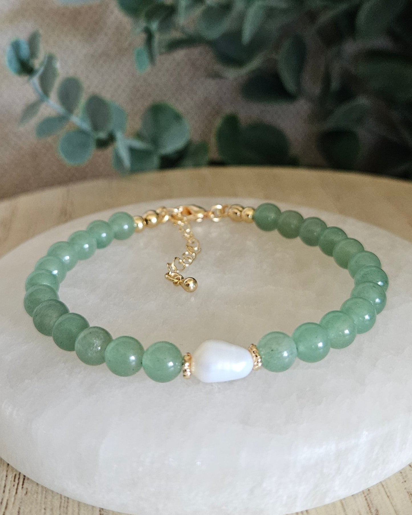 Green beaded bracelet with gold accents with a white pearl with greenery in the background