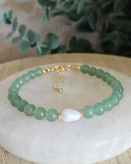 Green beaded bracelet with gold accents with a white pearl with greenery in the background