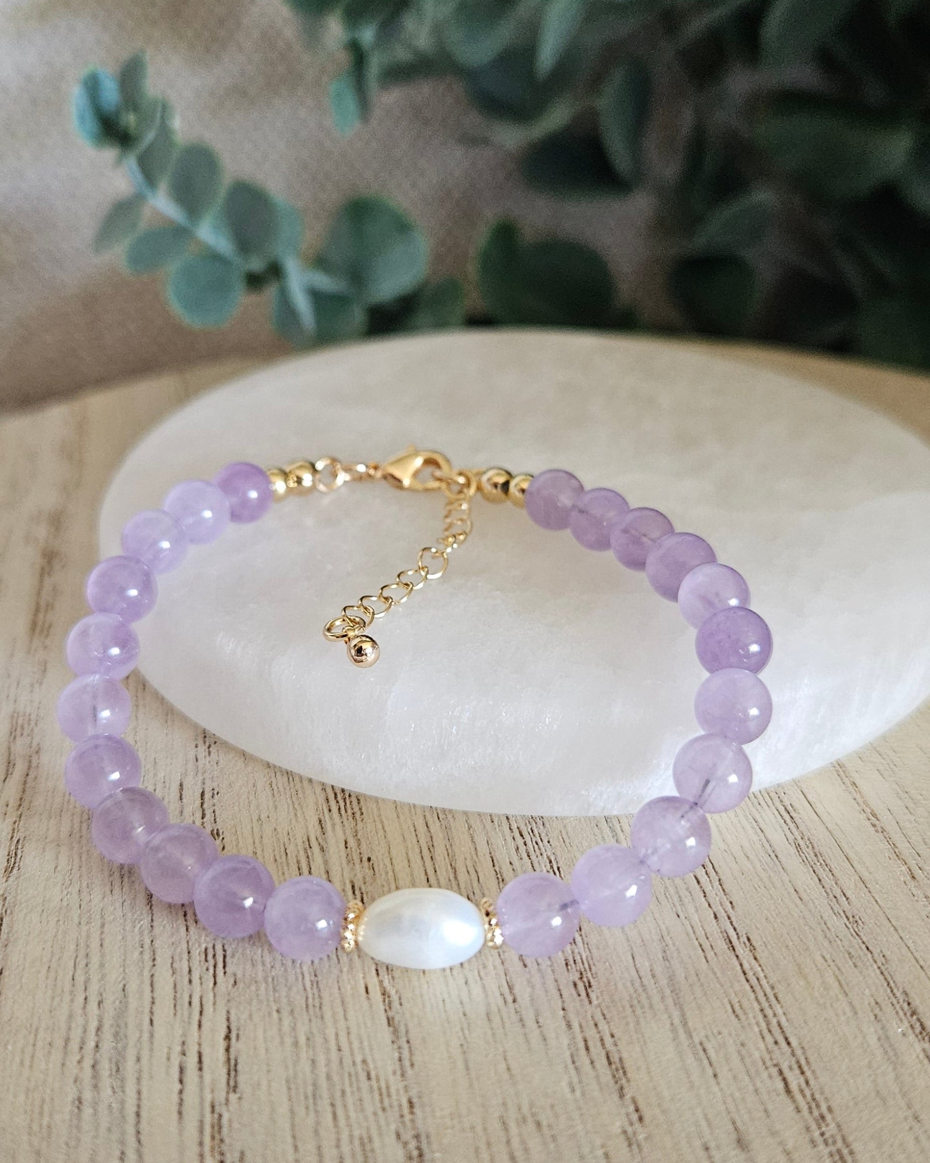 Purple beaded bracelet with a gold clasp on a wooden surface with greenery in the background