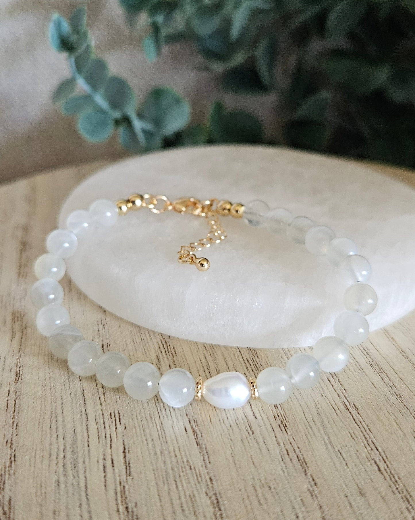 white moonstone bracelet with freshwater pearl focal on a selenite plate with greenery in background