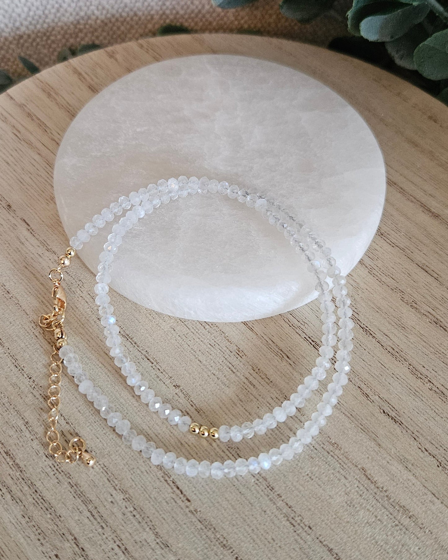 Overhead view of the faceted Moonstone necklace loosely coiled below a round selenite plate