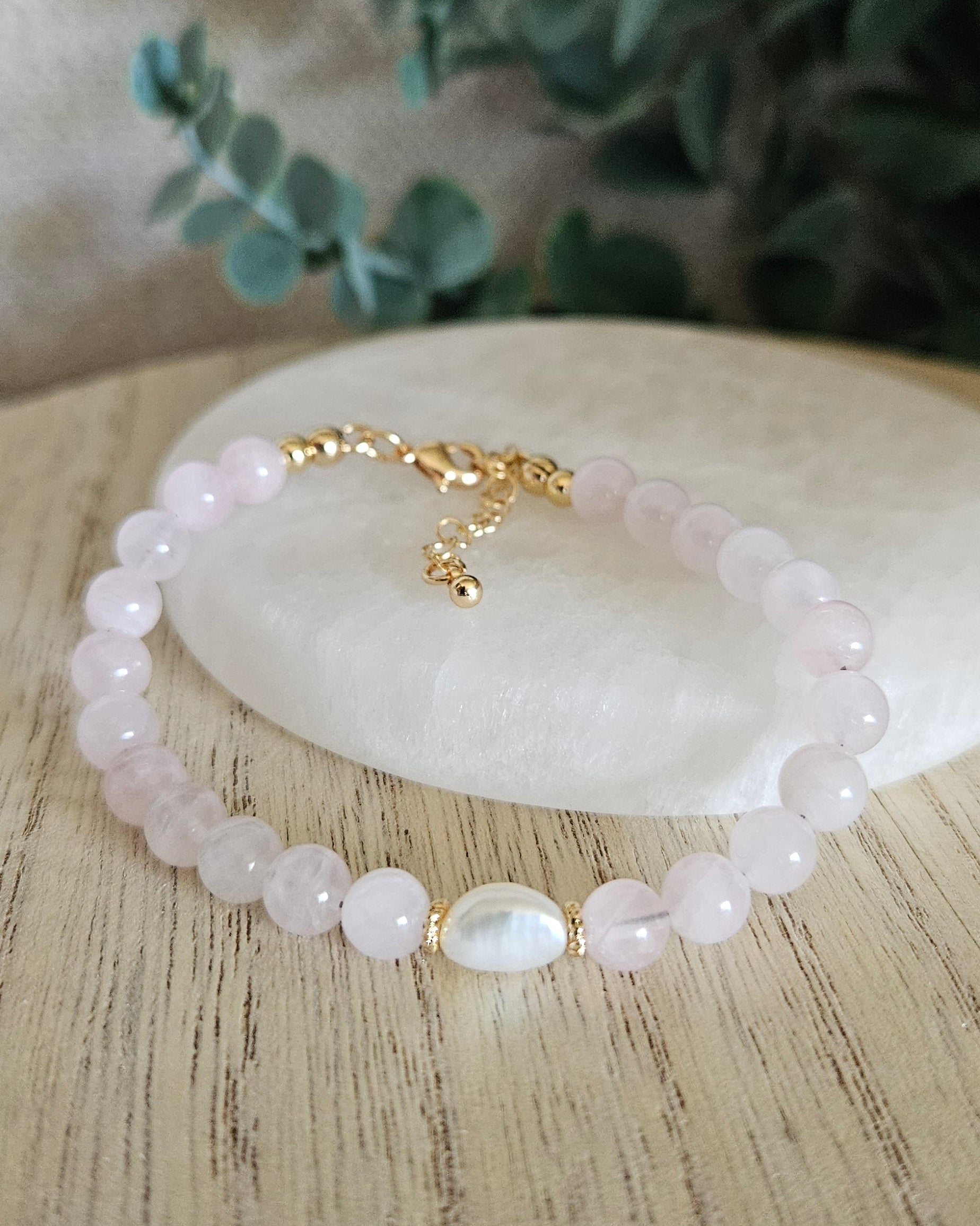 Rose Quartz Bracelet with a freshwater pearl focal and gold accents on selenite plate and greenery in the background