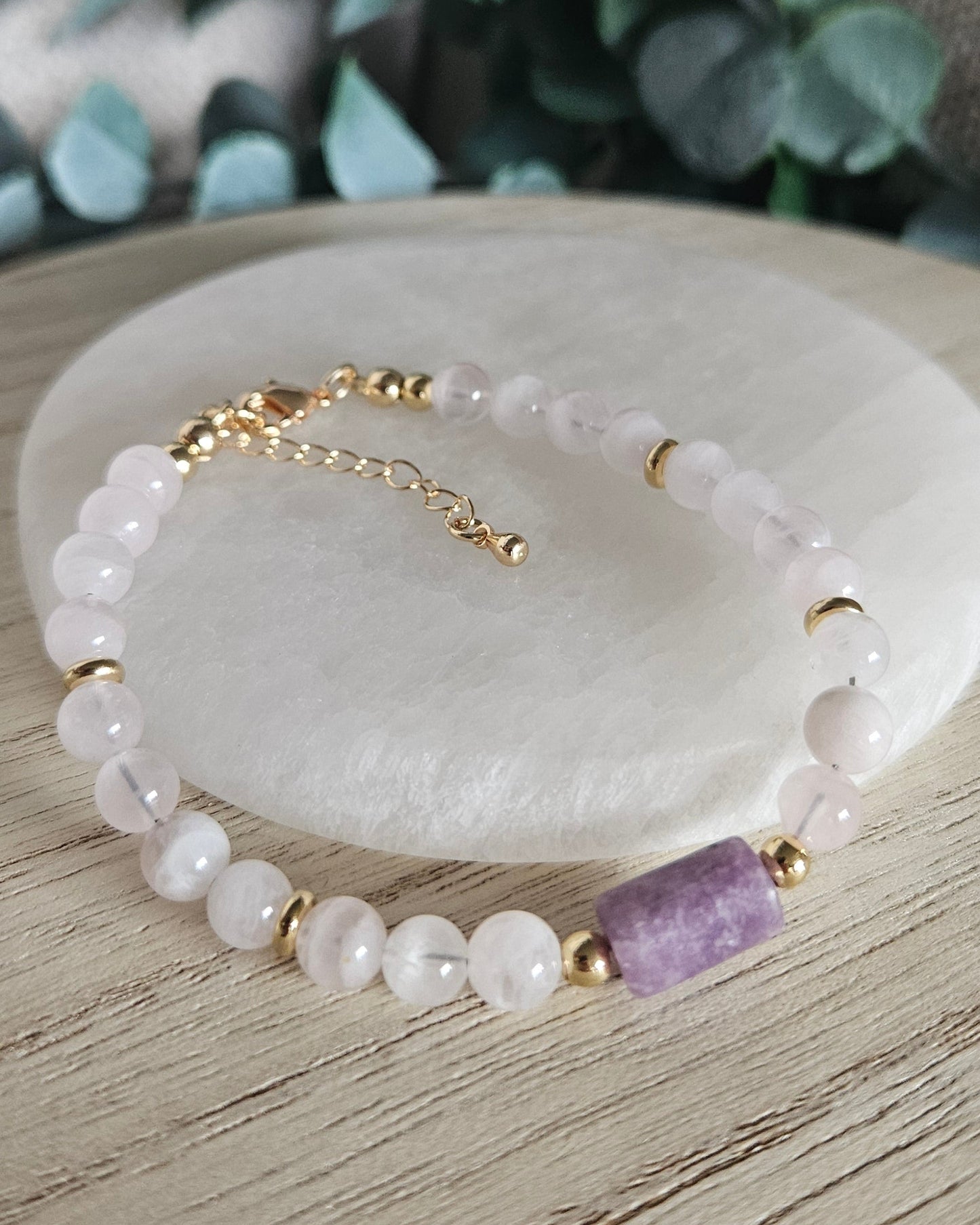 Rose Quartz and Lepidolite bracelet displayed on light wood beside a round selenite plate