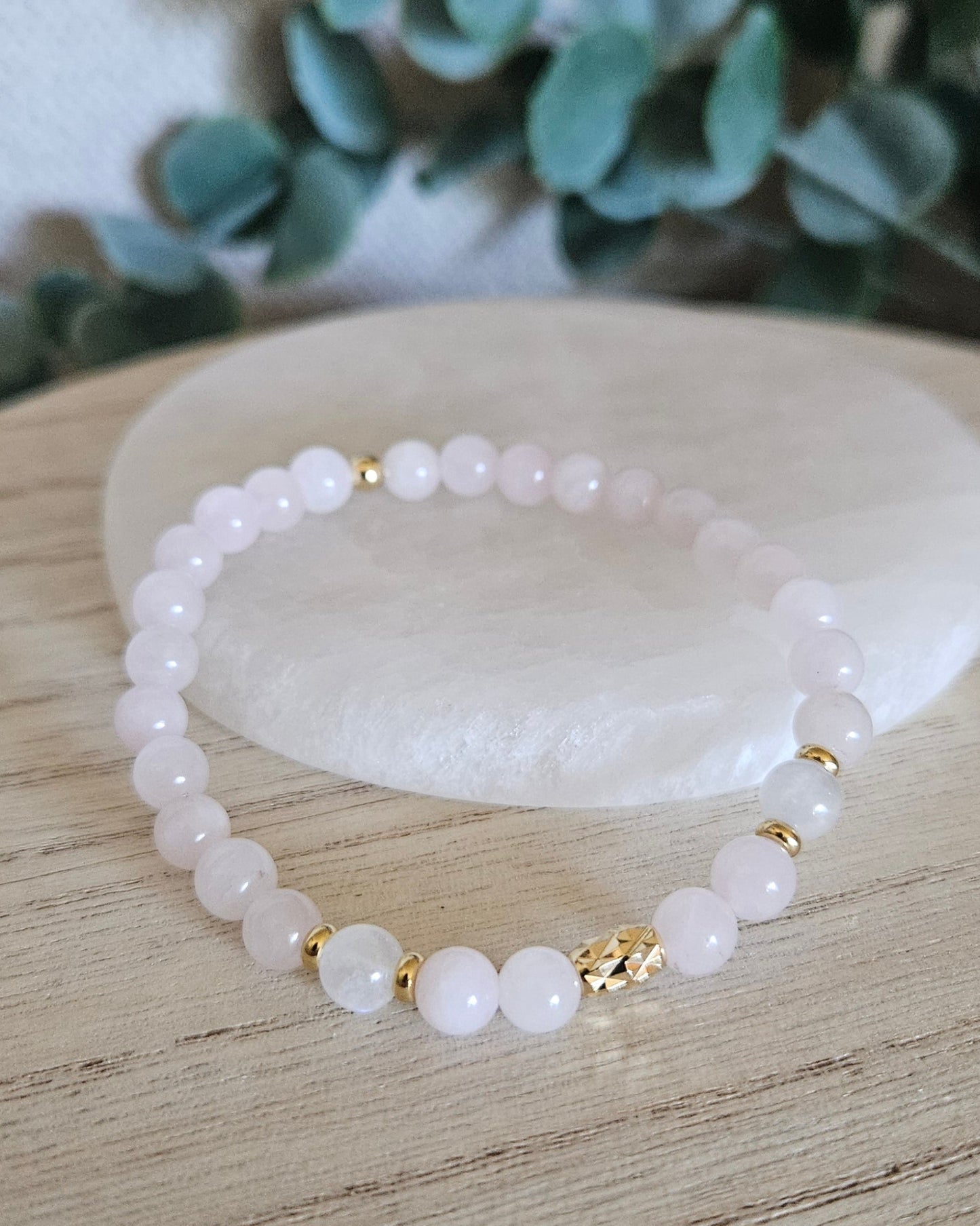 Rose Quartz and Moonstone bracelet arranged before a selenite plate with eucalyptus in the background