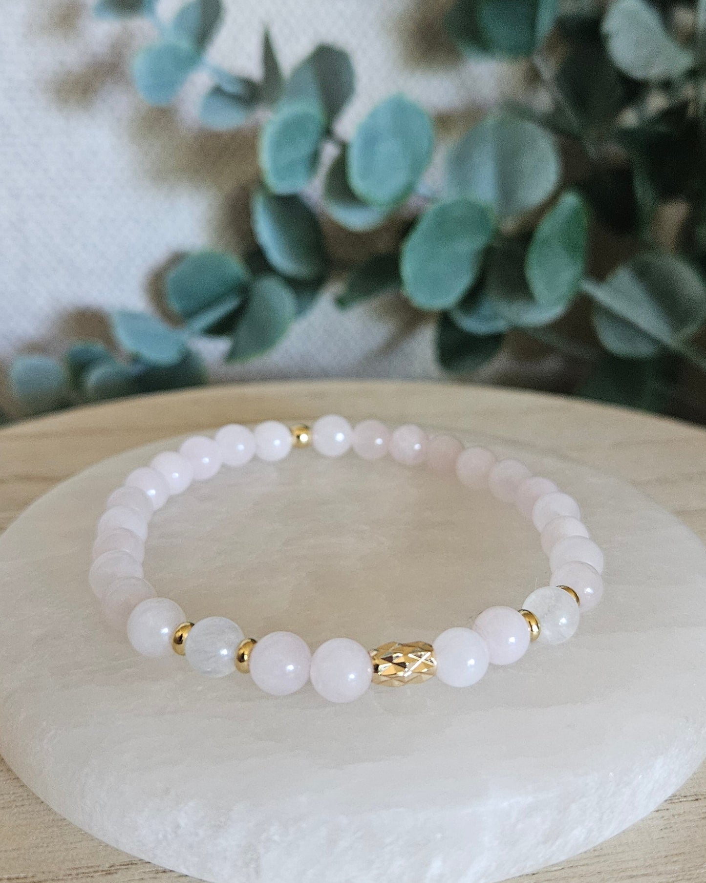 Rose Quartz and Moonstone stretch bracelet with gold accents displayed on a round selenite plate