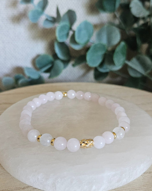 Rose Quartz and Moonstone stretch bracelet with gold accents displayed on a round selenite plate