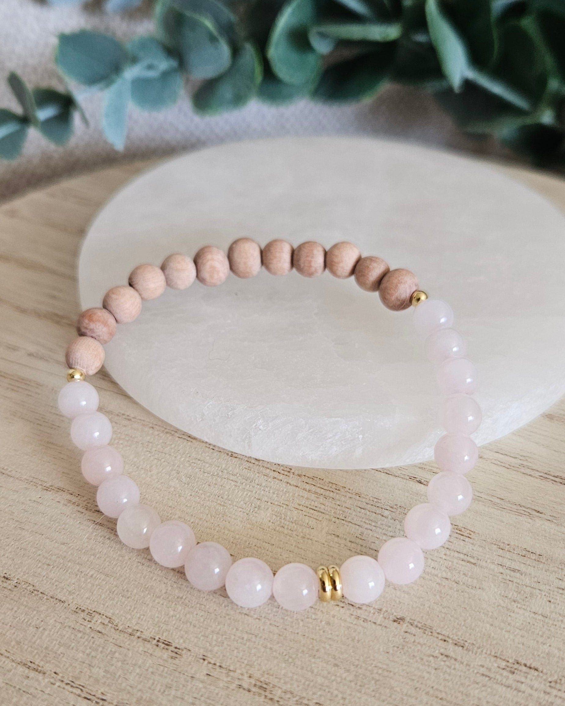Rose Quartz and unwaxed Rosewood diffuser bracelet with gold-plated accents displayed beside a selenite plate