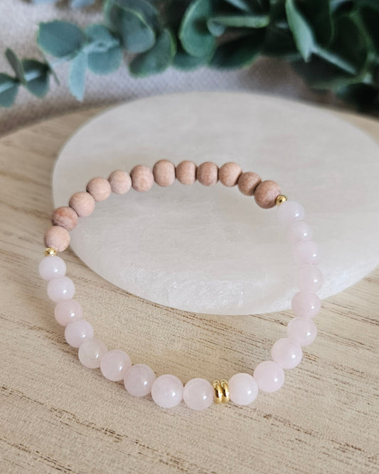 Rose Quartz and unwaxed Rosewood diffuser bracelet with gold-plated accents displayed beside a selenite plate
