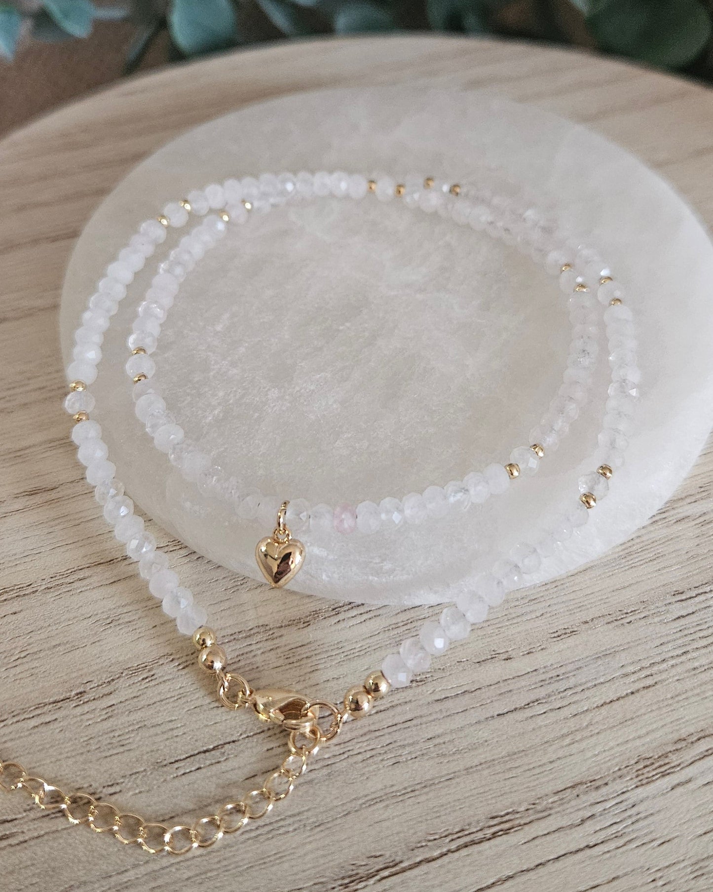 Rose Quartz heart necklace loosely coiled on selenite with its gold-plated clasp and extender chain visible