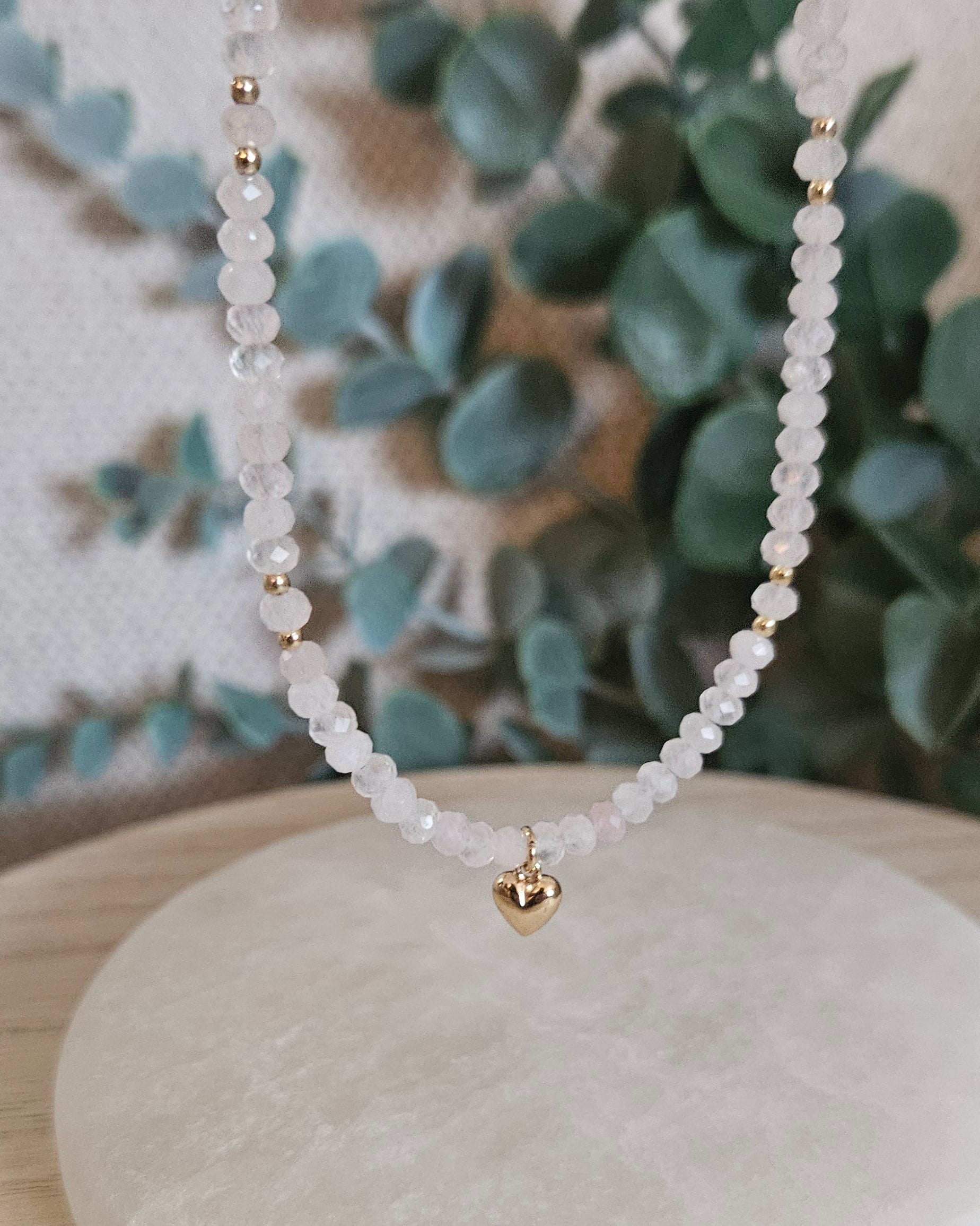 Rose Quartz necklace displayed upright with a gold-plated heart pendant centred against eucalyptus