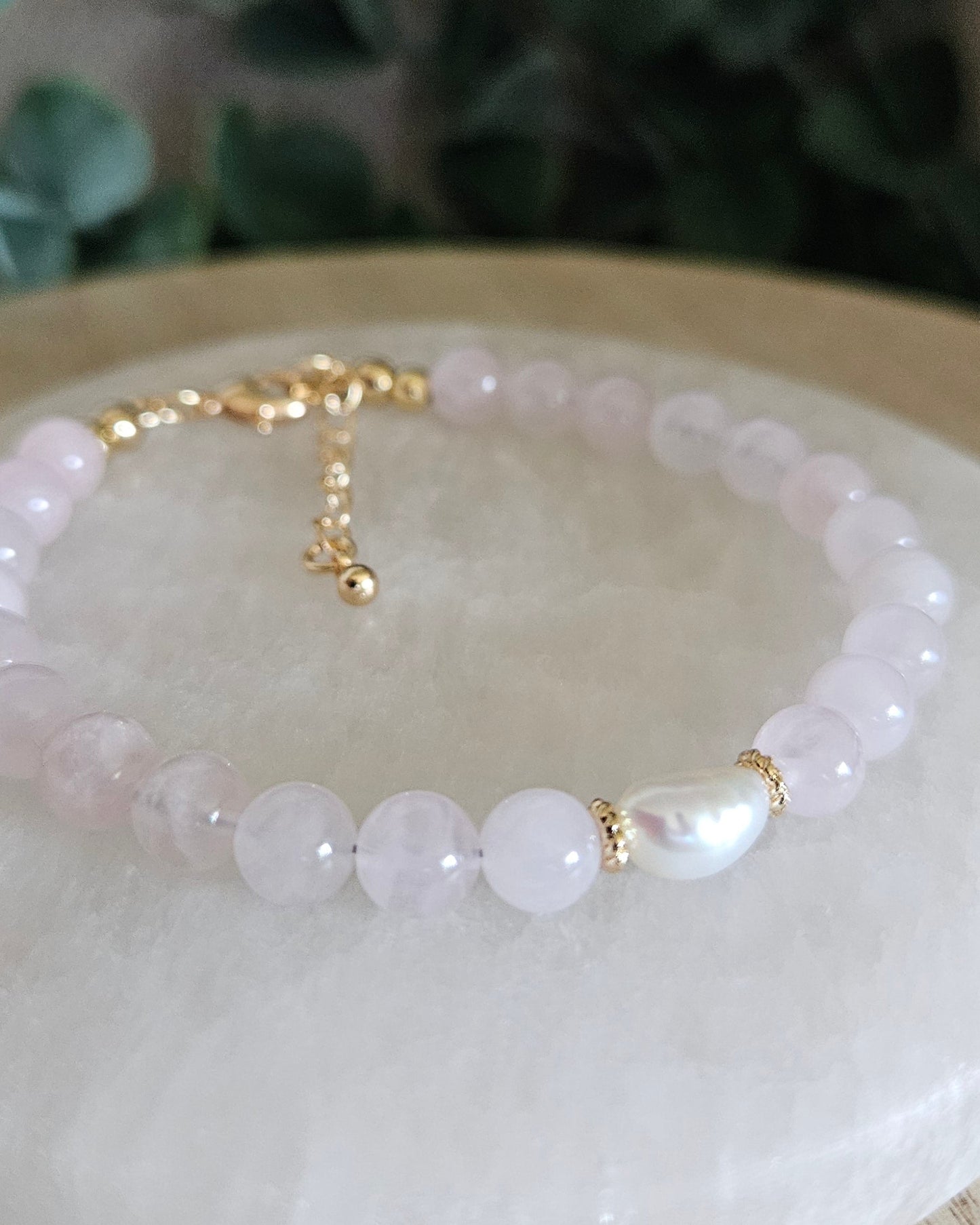 Rose Quartz Bracelet with a freshwater pearl focal and gold accents with greenery in the background